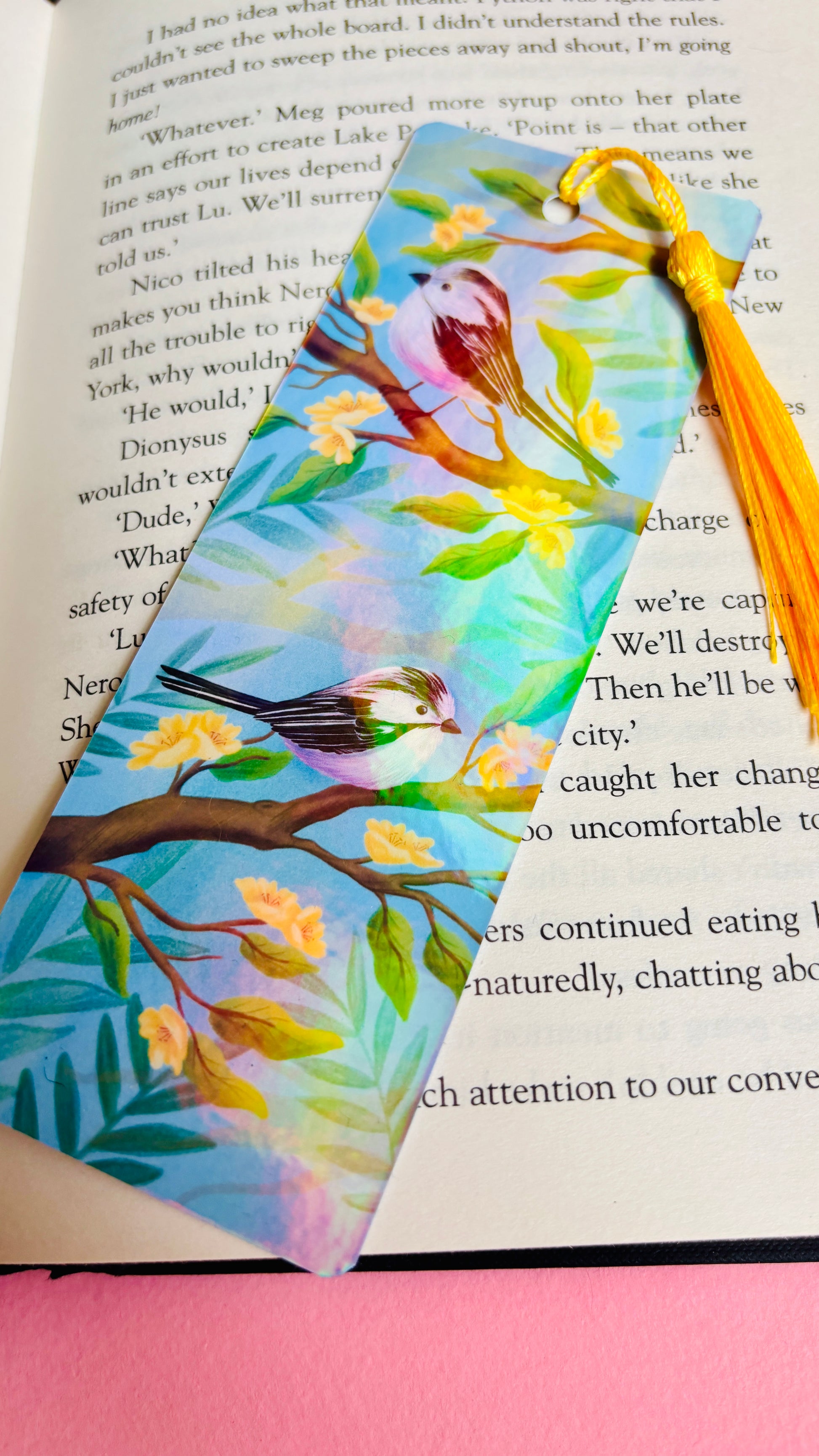 Handmade bookmark with illustration of two cute long tailed tits sitting on delicate branches surrounded by yellow flowers. Finished with rainbow holographic laminate, rounded corners and a tassel. Ideal gift for bookish gifts lovers.