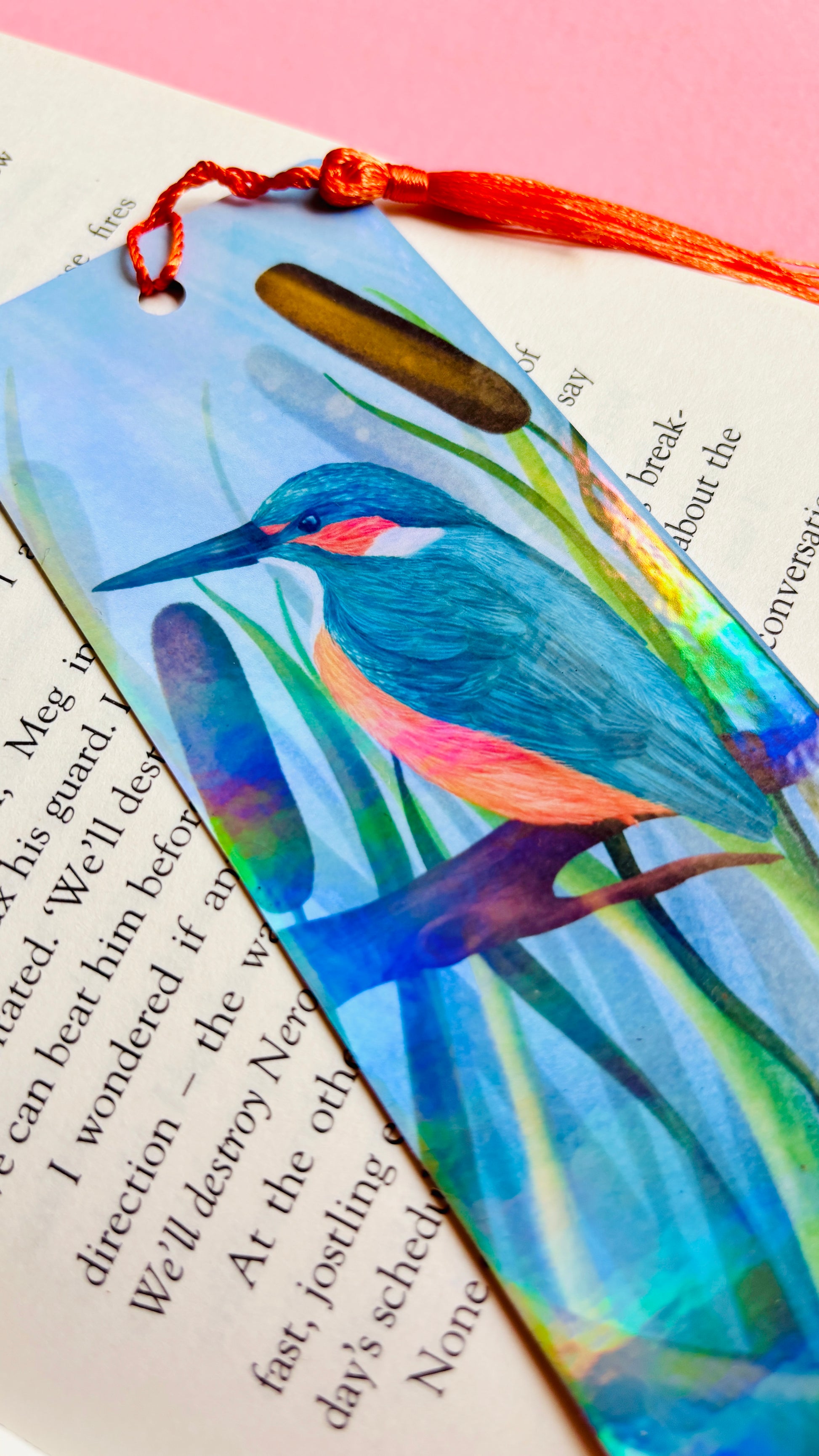 Handmade bookmark with a beautiful illustration of a kingfisher bird in the reads. This holographic bookmark has a rainbow laminate finish, tassel and rounded corners. Ideal for bookish gifts and nature lovers.