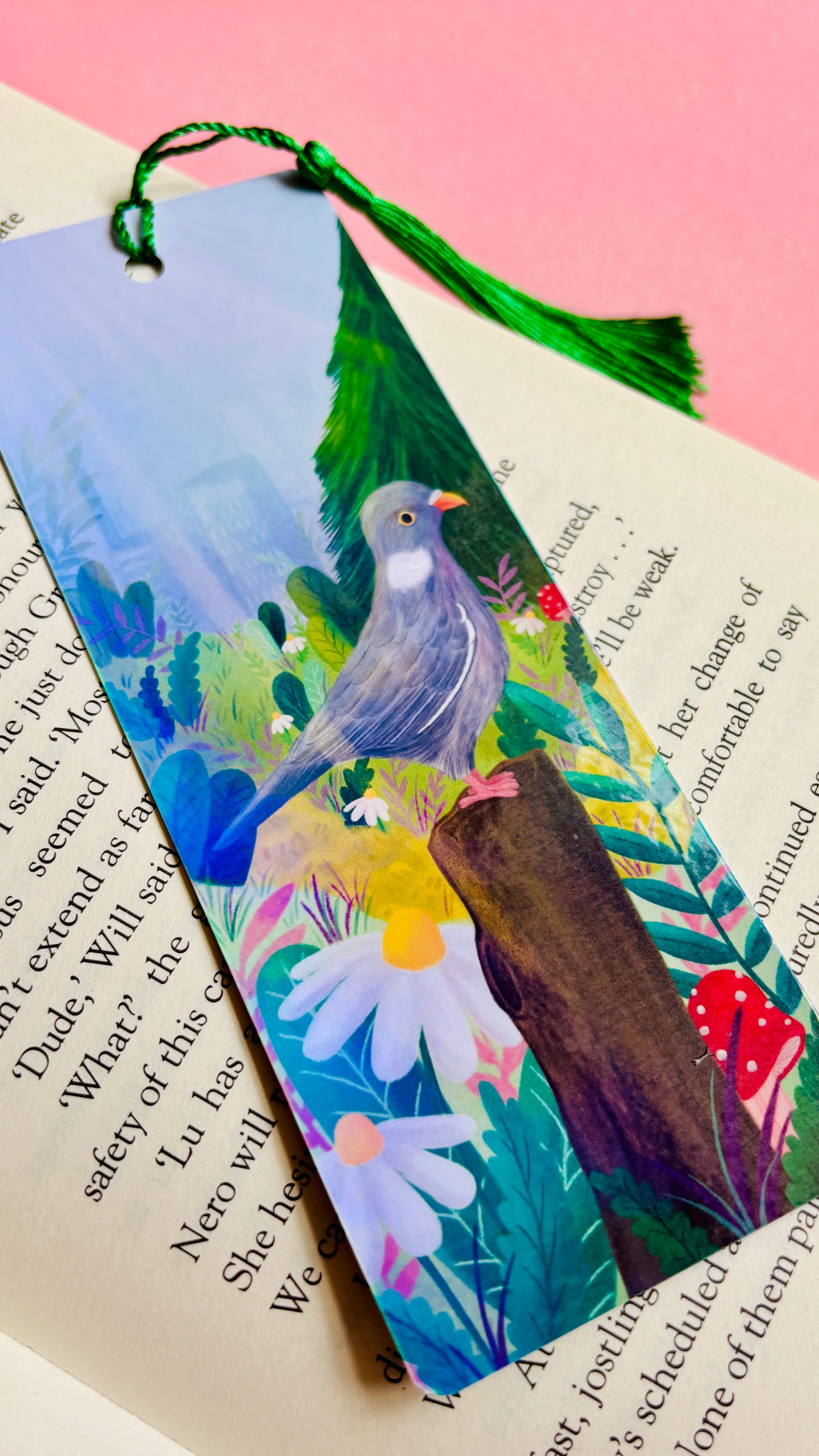 Handmade bookmark with cute pigeon art. This holographic bookmark features an adorable wood pigeon sitting on a mossy tree stump surrounded by colourful plants and flowers with a subtle cityscape in the background. Finished with a tassel, rounded corners and rainbow holographic laminate it makes a great gift for pigeon lovers and bookish besties.