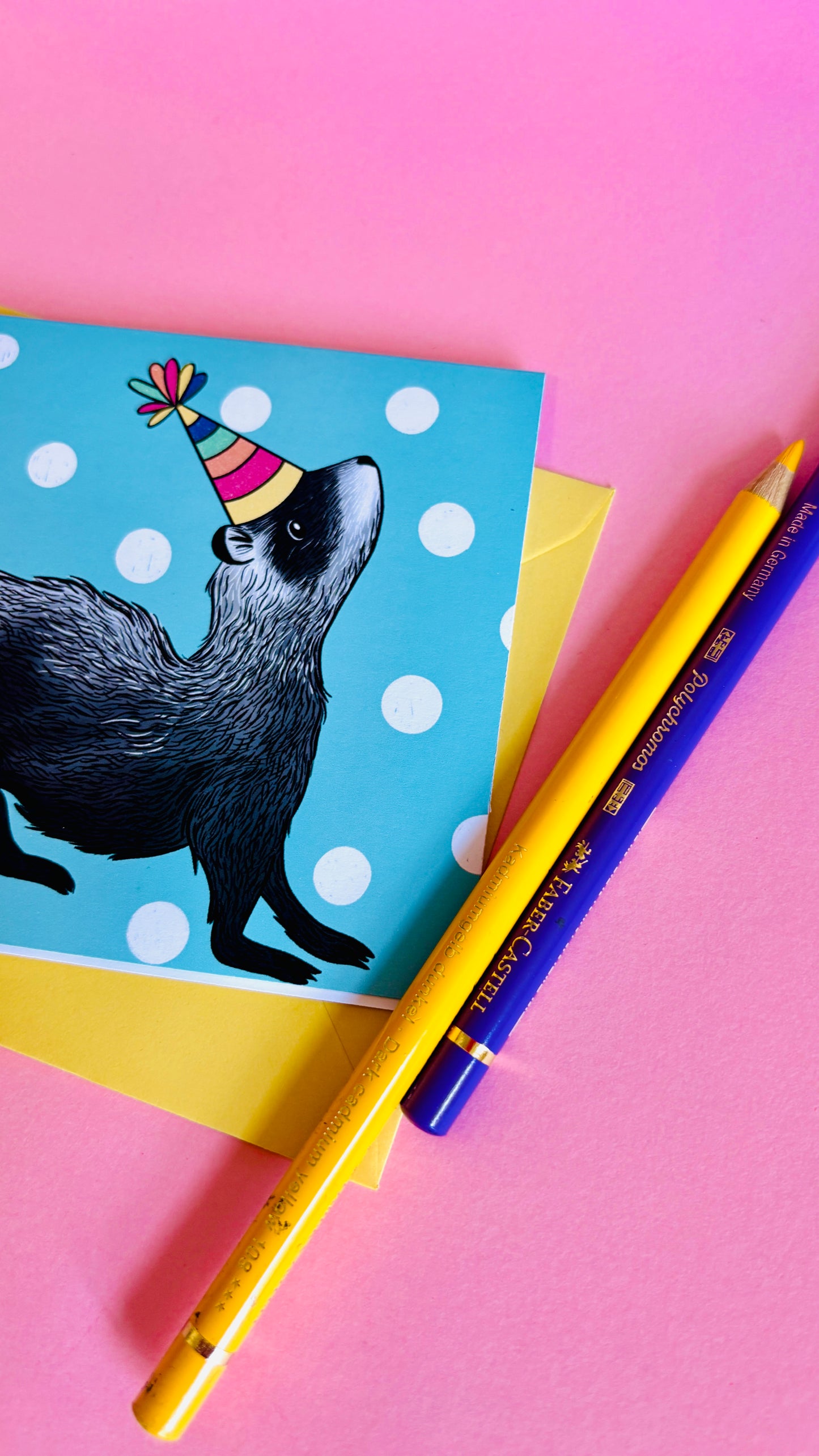 a colourful handmade ferret greetings card of a black and white ferret in a colourful party hat against a blue background with white polka dots