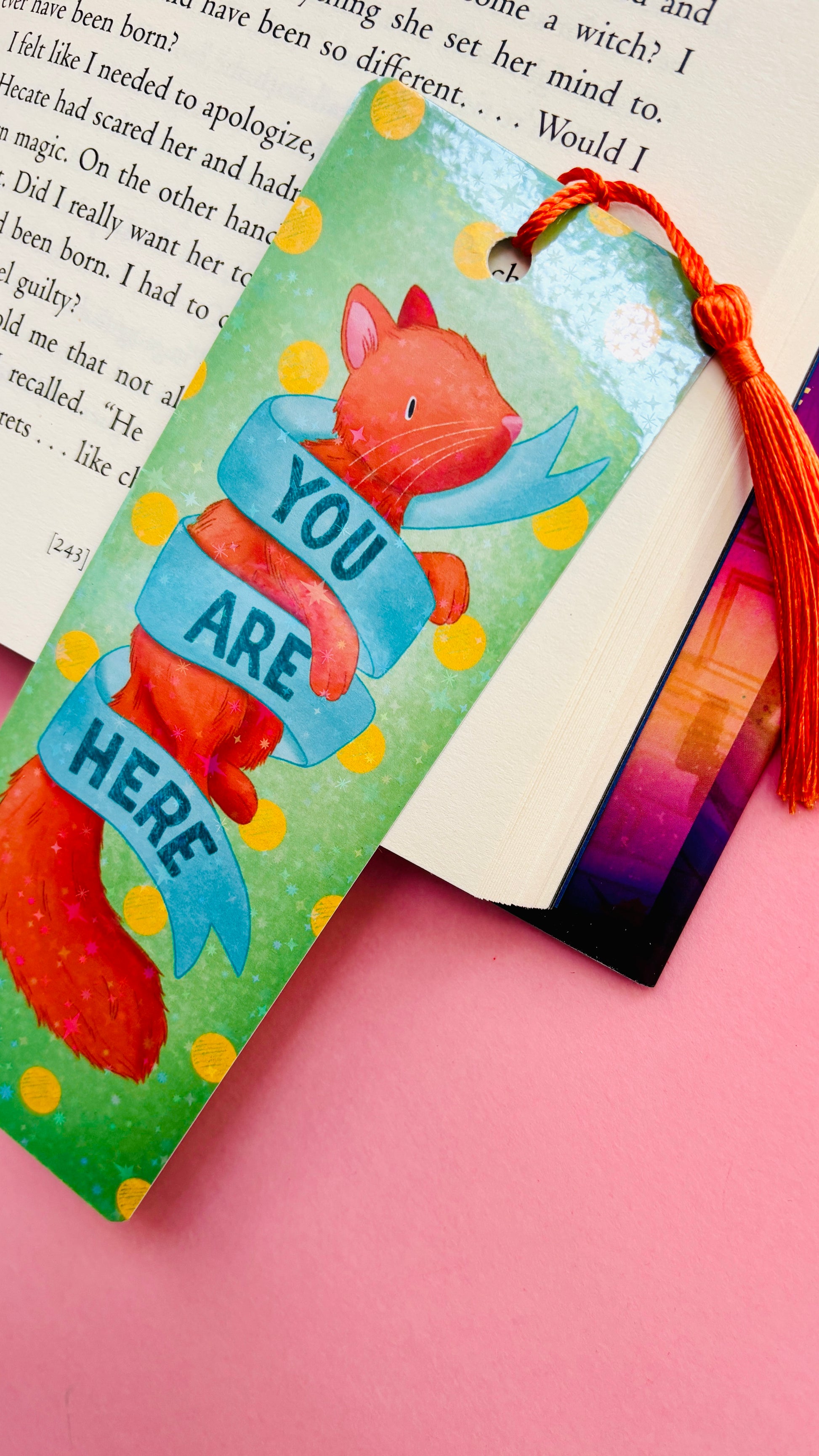 Handmade ginger cat bookmark with holographic rainbow finish, orange tassel, retro “You are here” banner, and green polka dot background, perfect for cat lovers and bookworms.