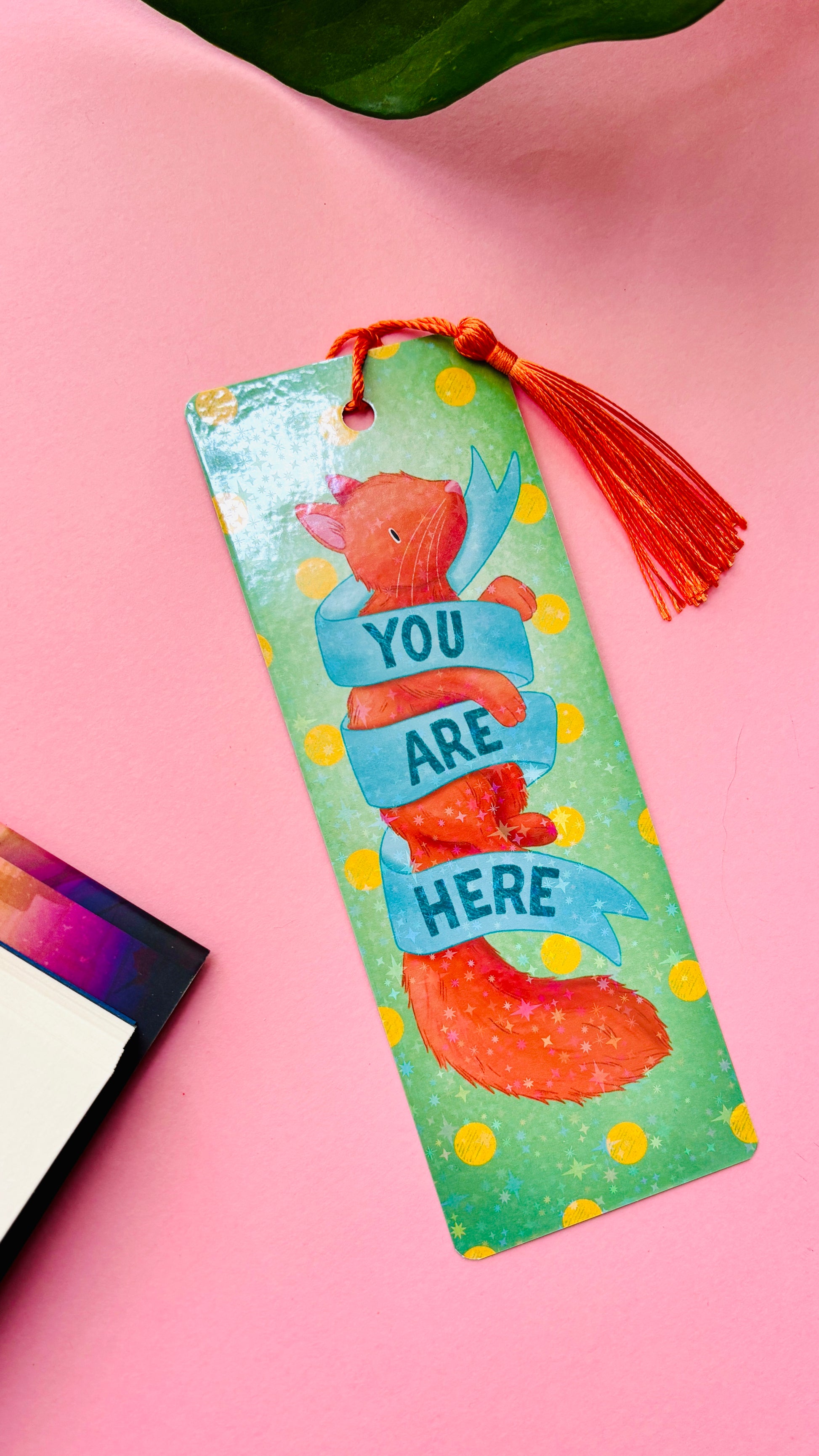 Hand-illustrated ginger cat bookmark featuring “You are here” banner, double-sided design, and rainbow holographic finish, ideal gift for cat lovers and readers.