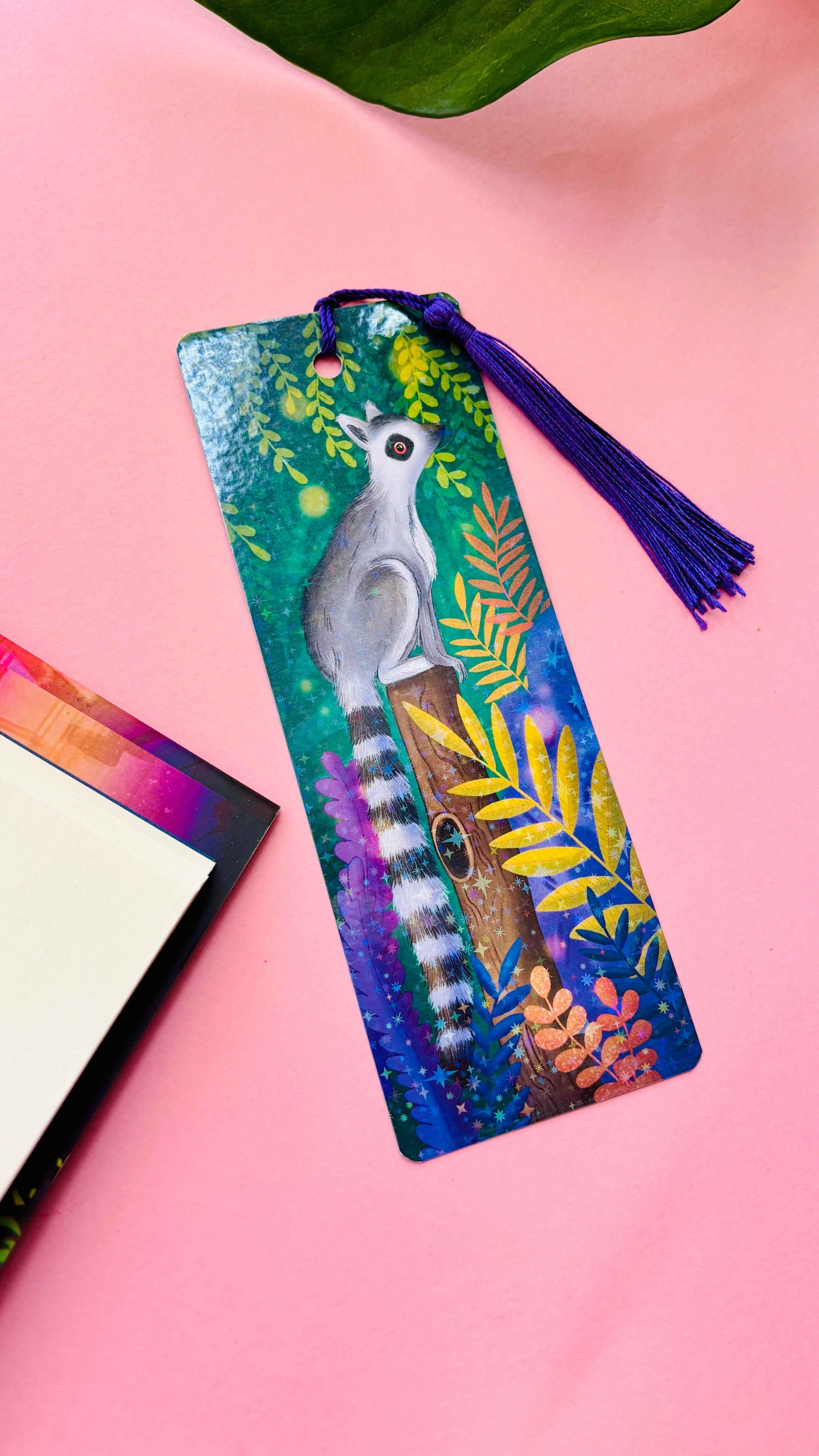 Handmade holographic bookmark featuring a hand-illustrated ring-tailed lemur in a tropical rainforest – with purple tassel.