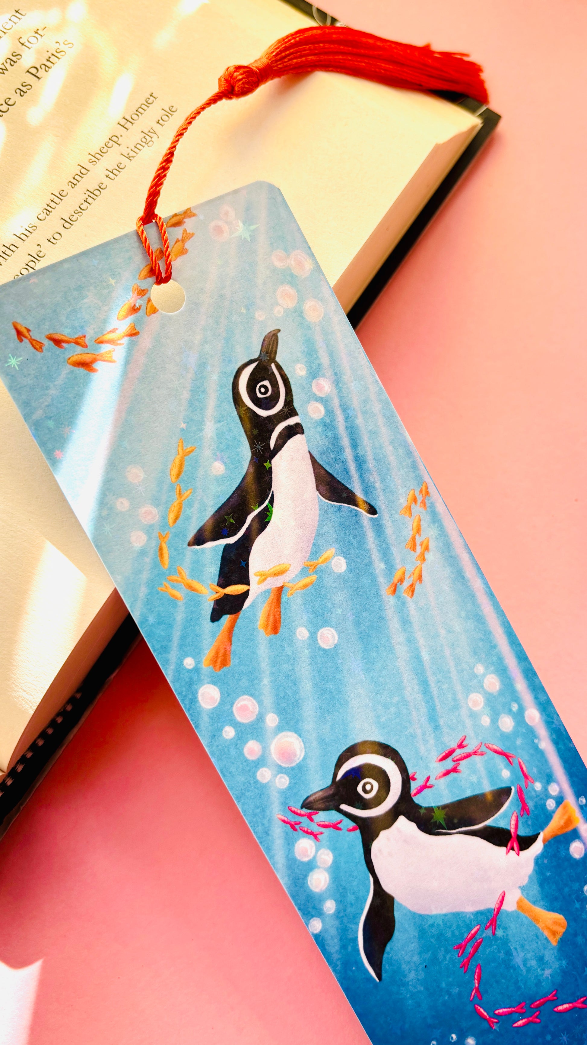 Handmade Humboldt penguin bookmark with rainbow holographic finish, featuring two penguins swimming in a sparkling ocean with colorful fish, perfect for book lovers and marine life enthusiasts.
