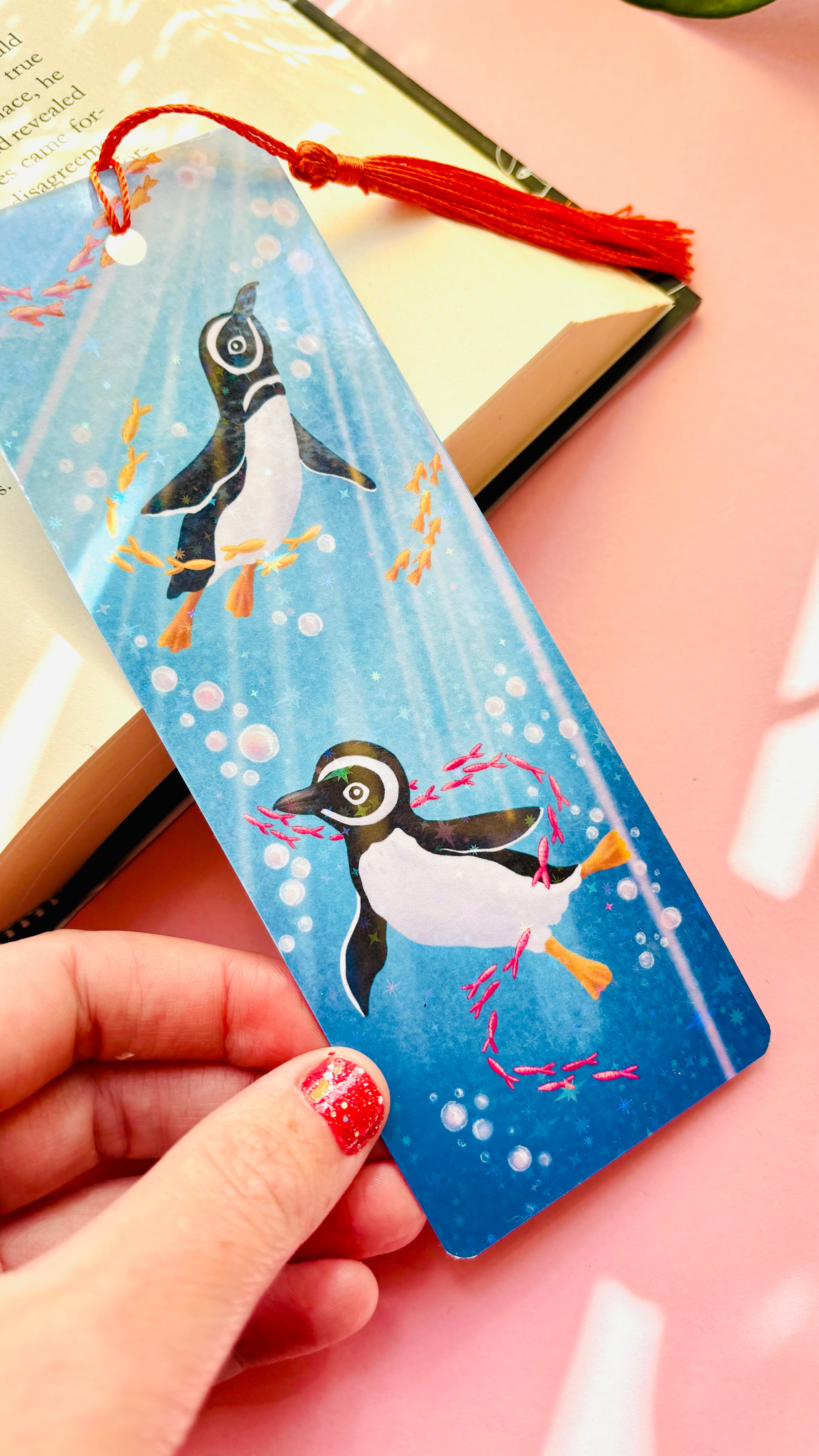 Handmade Humboldt penguin bookmark with rainbow holographic finish, featuring two penguins swimming in a sparkling ocean with colorful fish, perfect for book lovers and marine life enthusiasts.