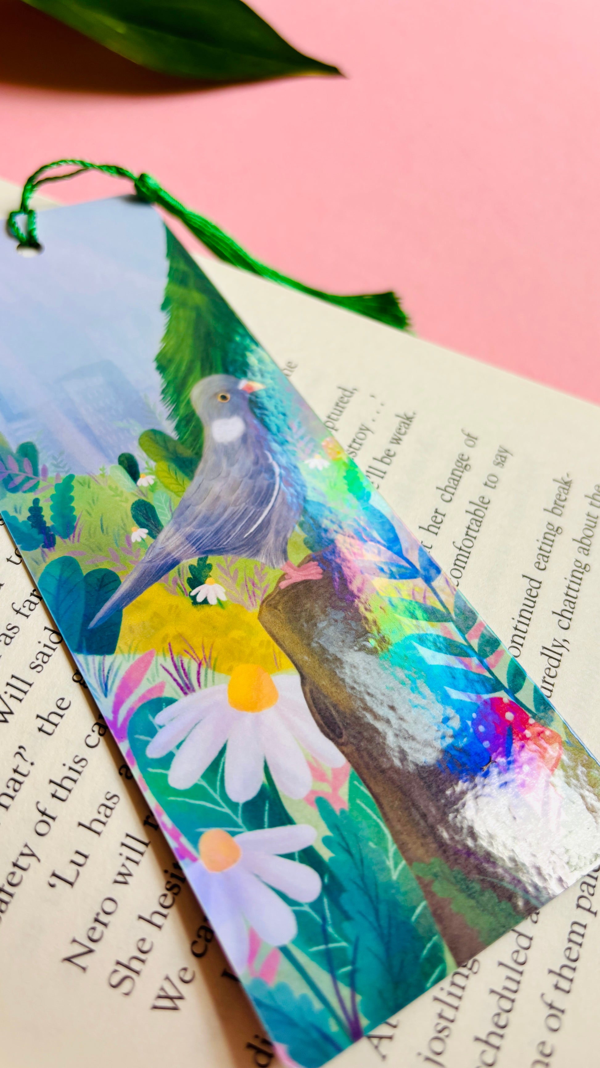 Handmade bookmark with cute pigeon art. This holographic bookmark features an adorable wood pigeon sitting on a mossy tree stump surrounded by colourful plants and flowers with a subtle cityscape in the background. Finished with a tassel, rounded corners and rainbow holographic laminate it makes a great gift for pigeon lovers and bookish besties.