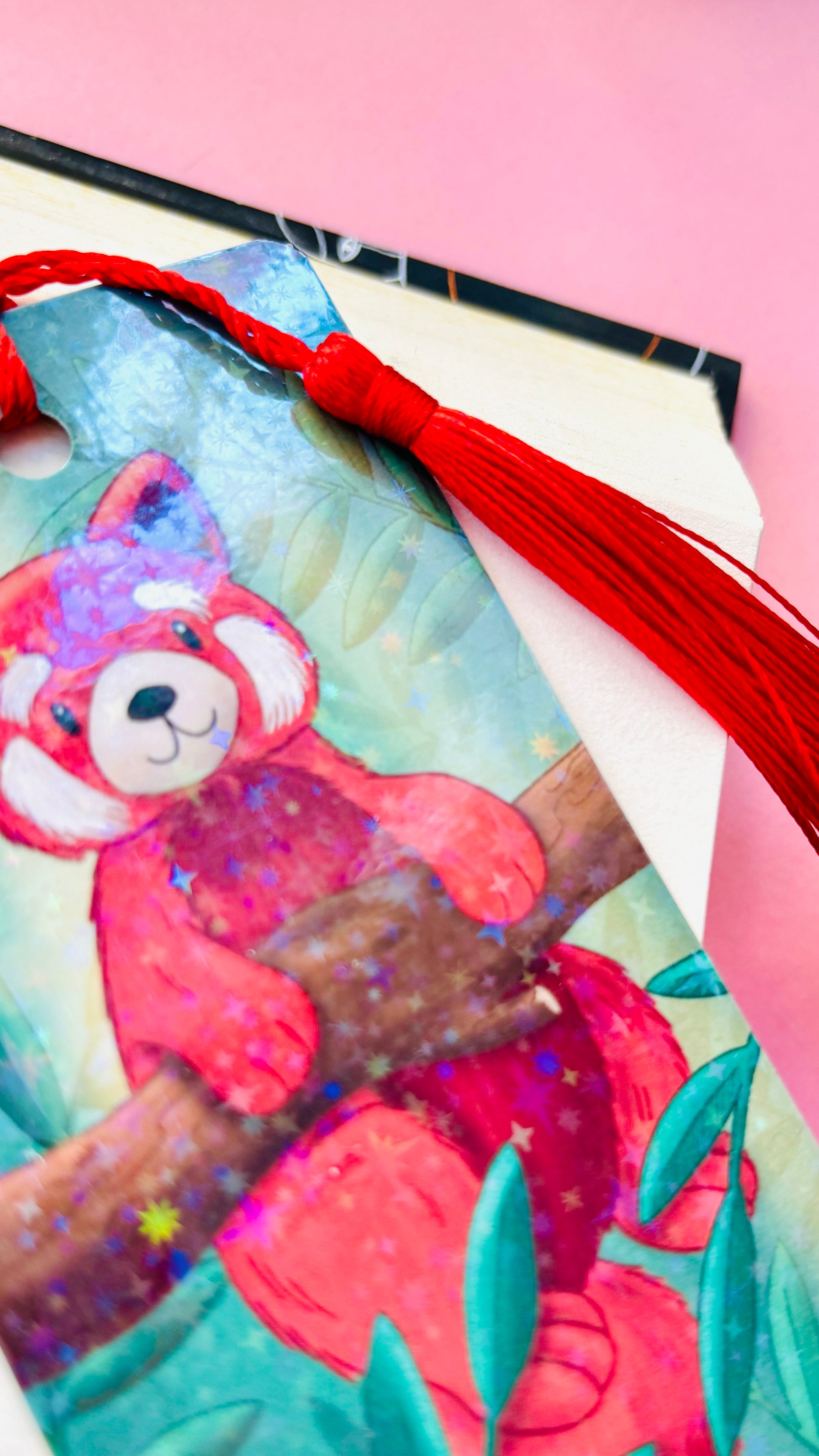 Cute red panda bookmark featuring a whimsical illustration, rainbow holographic laminate, and green tassel, perfect for animal lovers and avid readers.