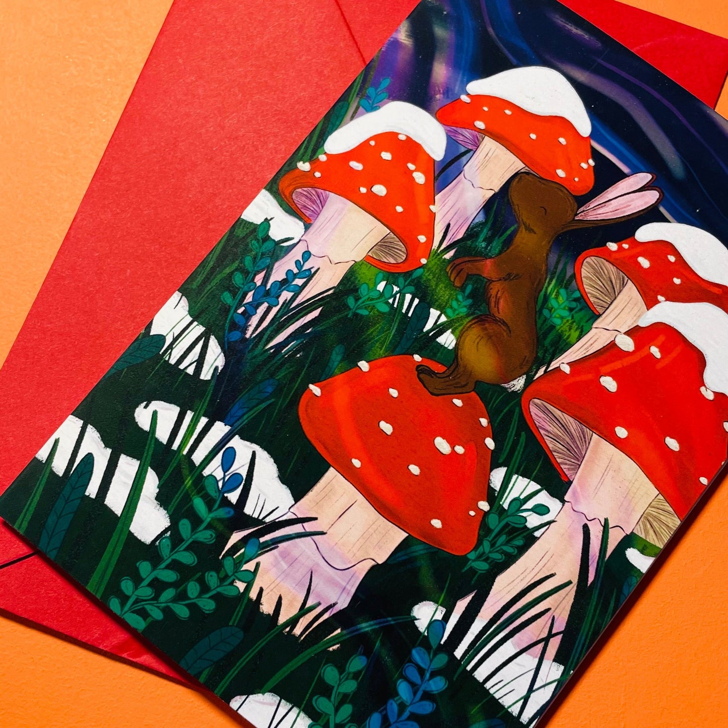 An adorable atmospheric greetings card of a tiny rabbit atop a snowy toadstool
