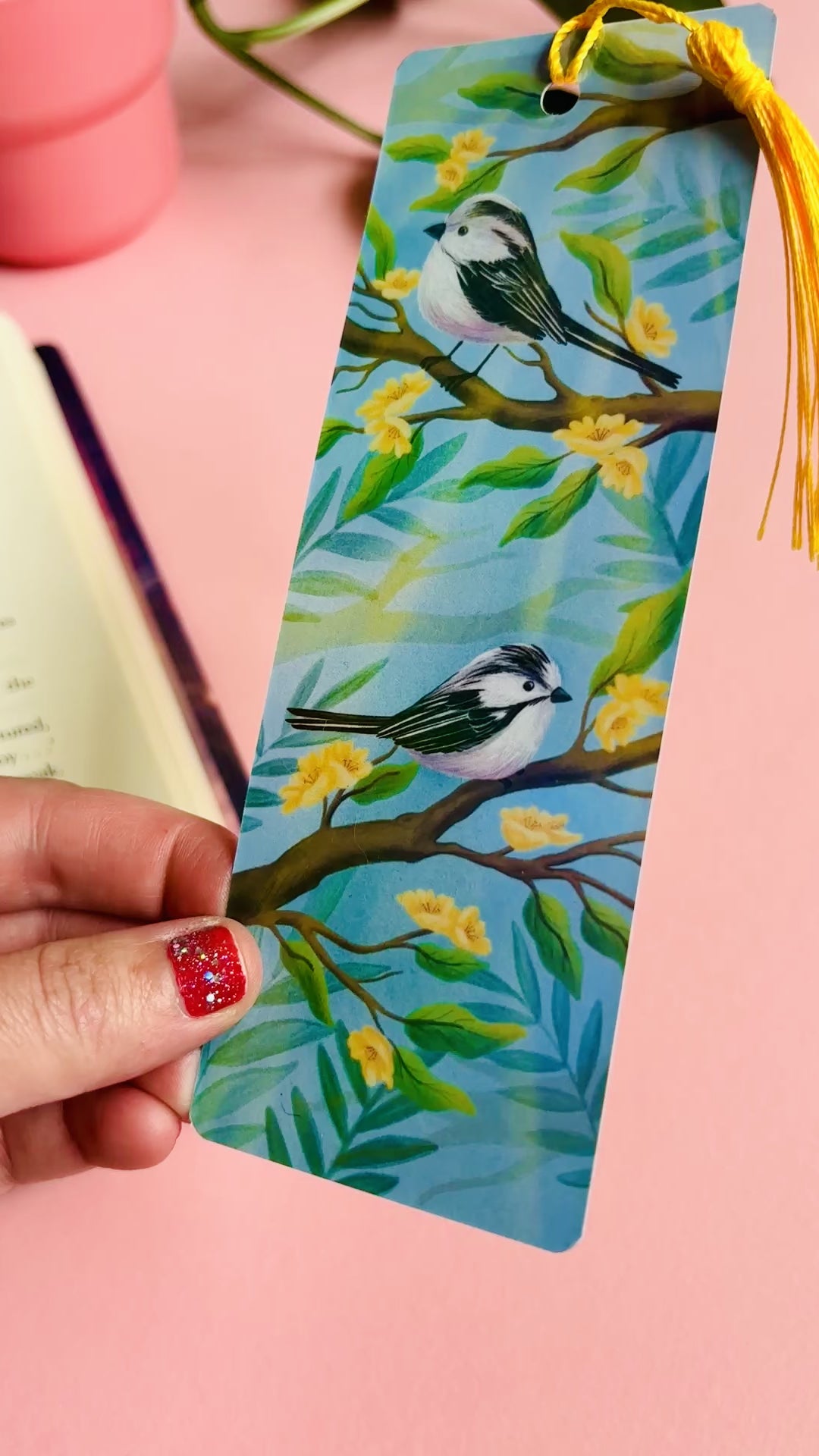 Handmade bookmark with illustration of two cute long tailed tits sitting on delicate branches surrounded by yellow flowers. Finished with rainbow holographic laminate, rounded corners and a tassel. Ideal gift for bookish gifts lovers.