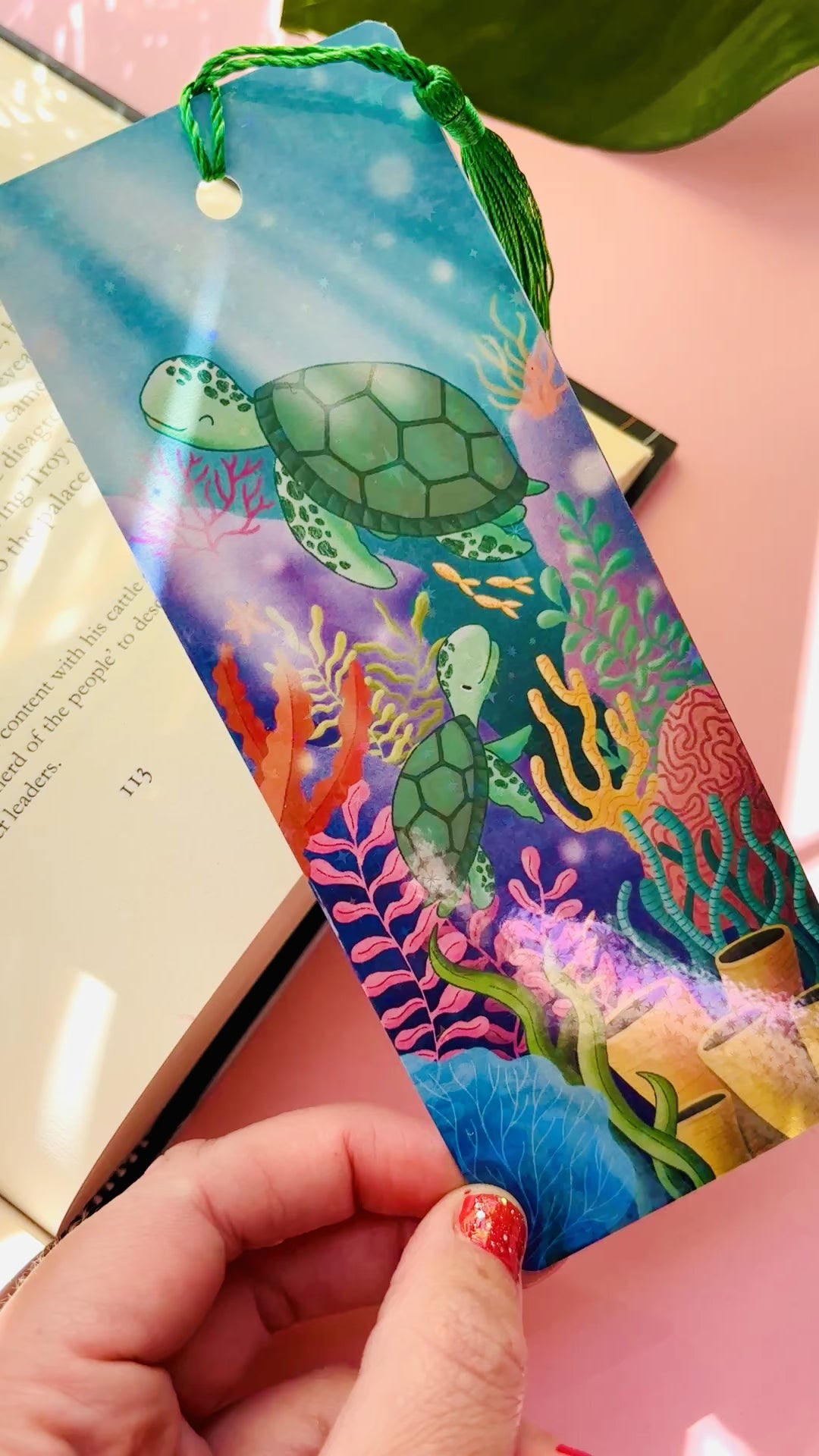 Ocean-inspired bookmark featuring two cute sea turtles swimming through a colorful coral reef, double-sided with rainbow holographic laminate and green tassel, perfect for readers and marine life fans.