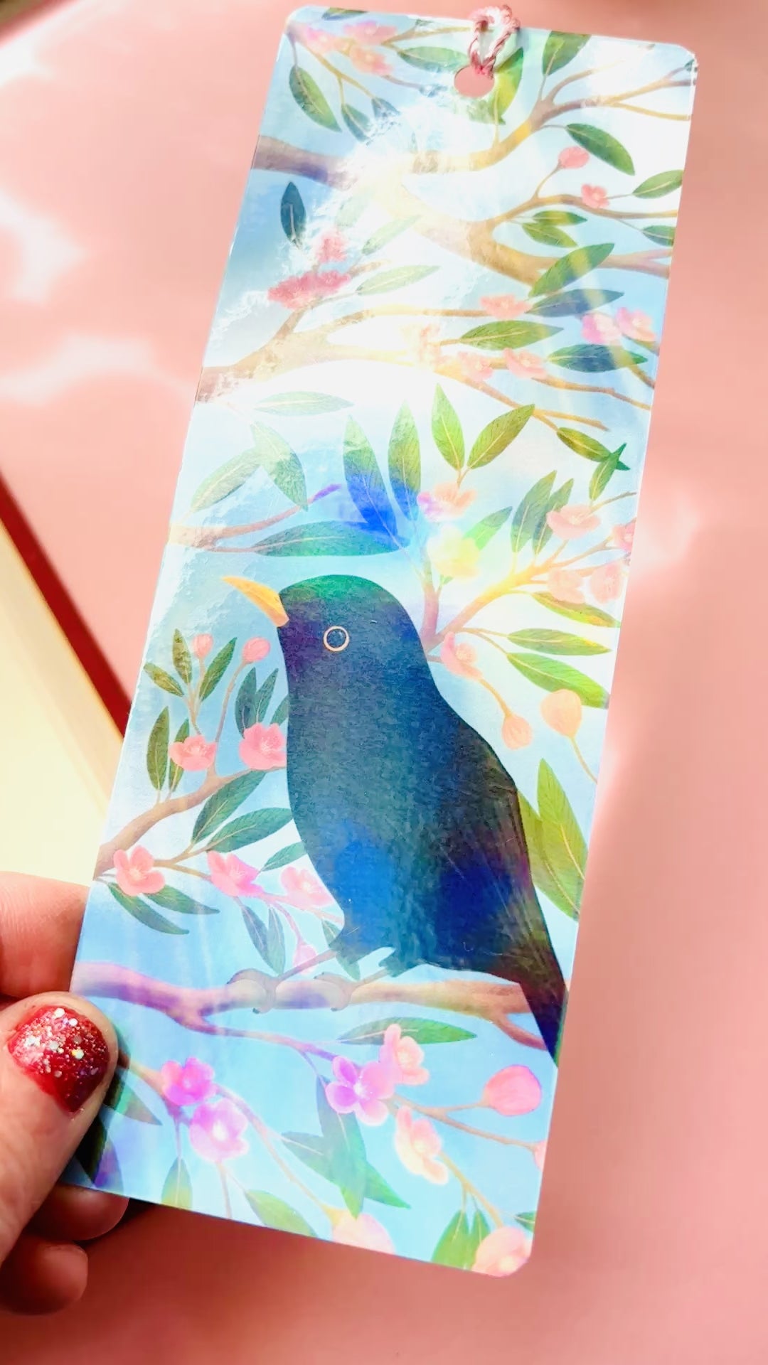 Handmade bookmark of blackbird in cherry blossom tree. Finished with rainbow holographic laminate, rounded corners and tassel.