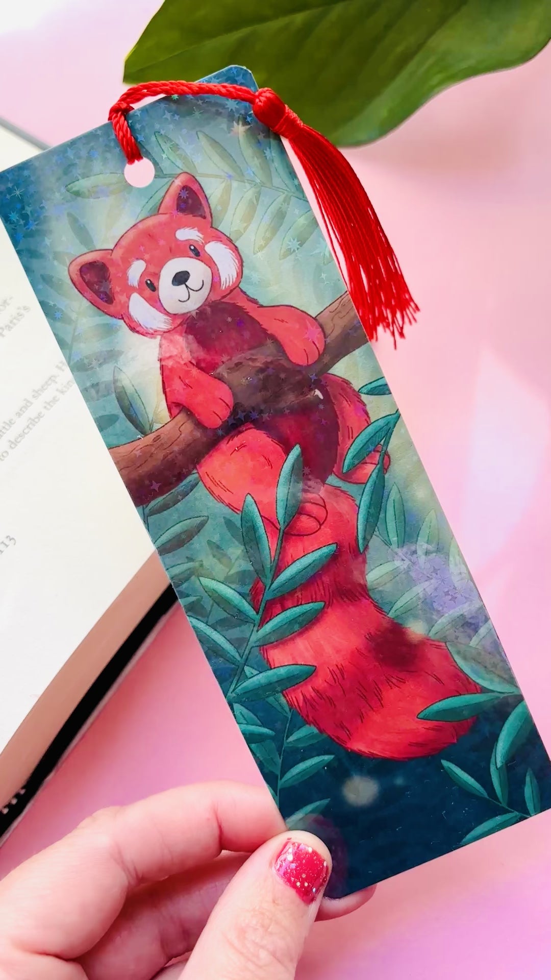 Cute red panda bookmark featuring a whimsical illustration, rainbow holographic laminate, and green tassel, perfect for animal lovers and avid readers.