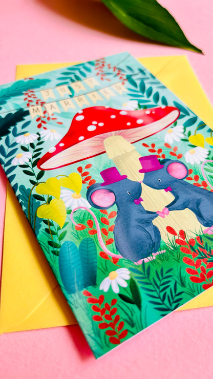Cute gay wedding card of two mice under a whimsical toadstool in a vibrant woodland setting full of flowers and plants. This handmade card is blank on the inside for your message a d supplied with a yellow envelope 