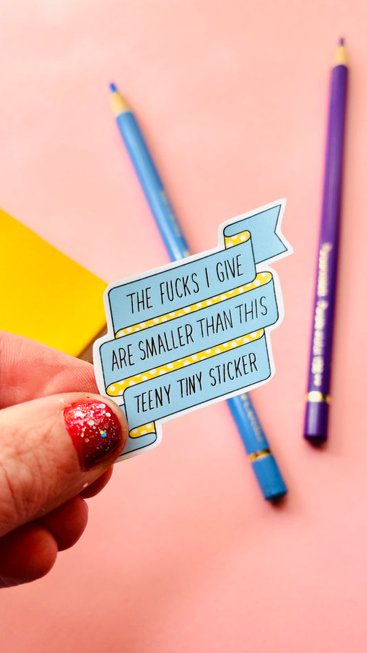 Small Sweary sticker reads “the fucks I give are smaller than this teeny tiny y sticker” on a blue and white polka dot background 