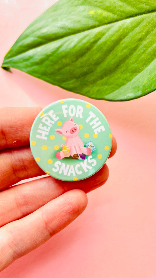 Cute pink pig badge surrounded by snacks, perfect for snack lovers and animal fans, available as magnet or pin.
