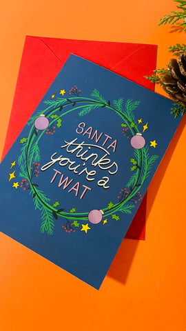 Santa thinks you’re a twat illustrated Christmas card on a dark background with the text surrounded by a festive wreath