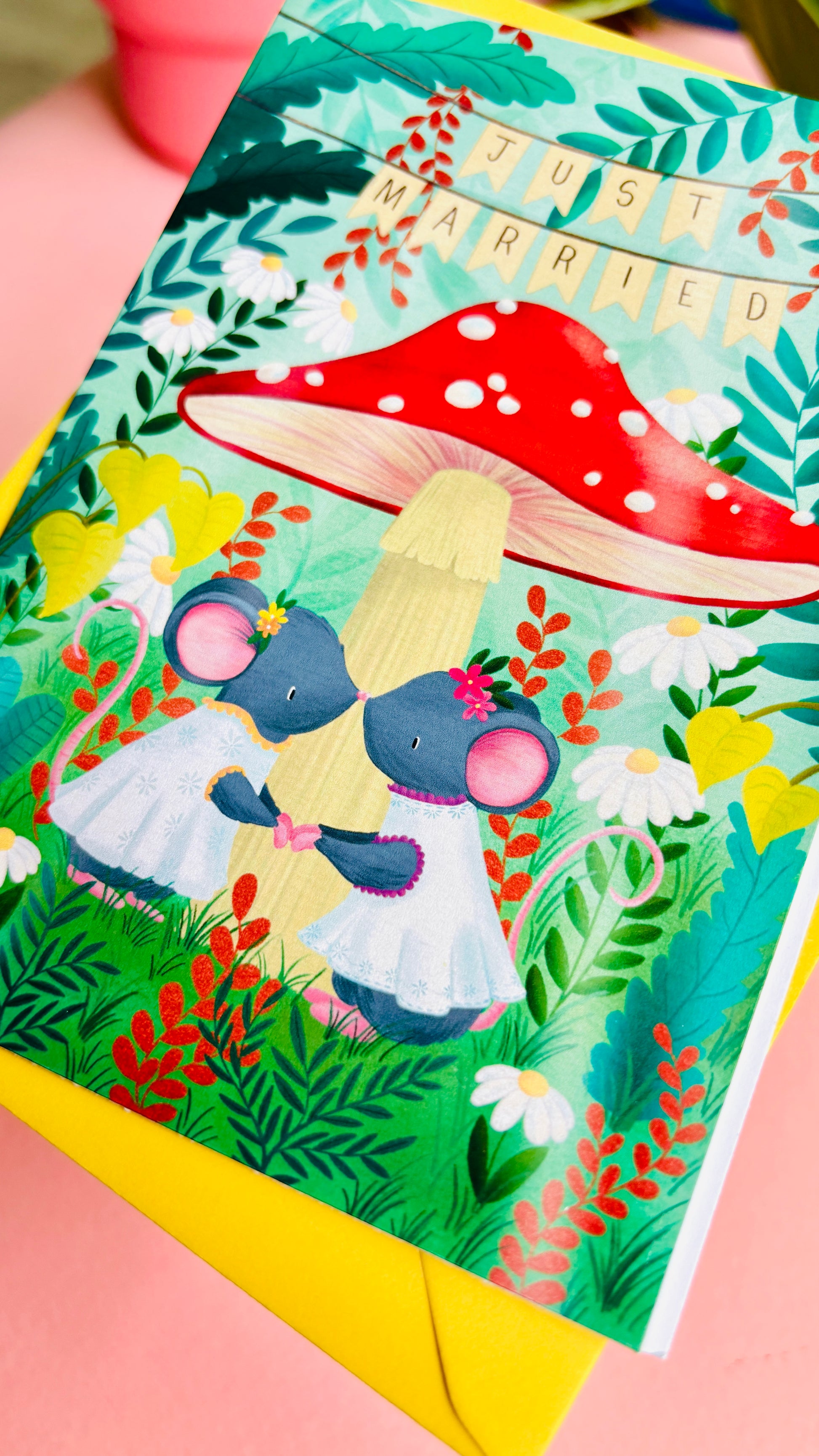 Handmade lesbian wedding card of two mice under a whimsical toadstool in a vibrant woodland setting full of flowers and plants. This handmade card is blank on the inside for your message a d supplied with a yellow envelope 
