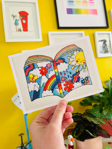 Hand embroidered art print of a book made from rainbows, sunshine and flowers.