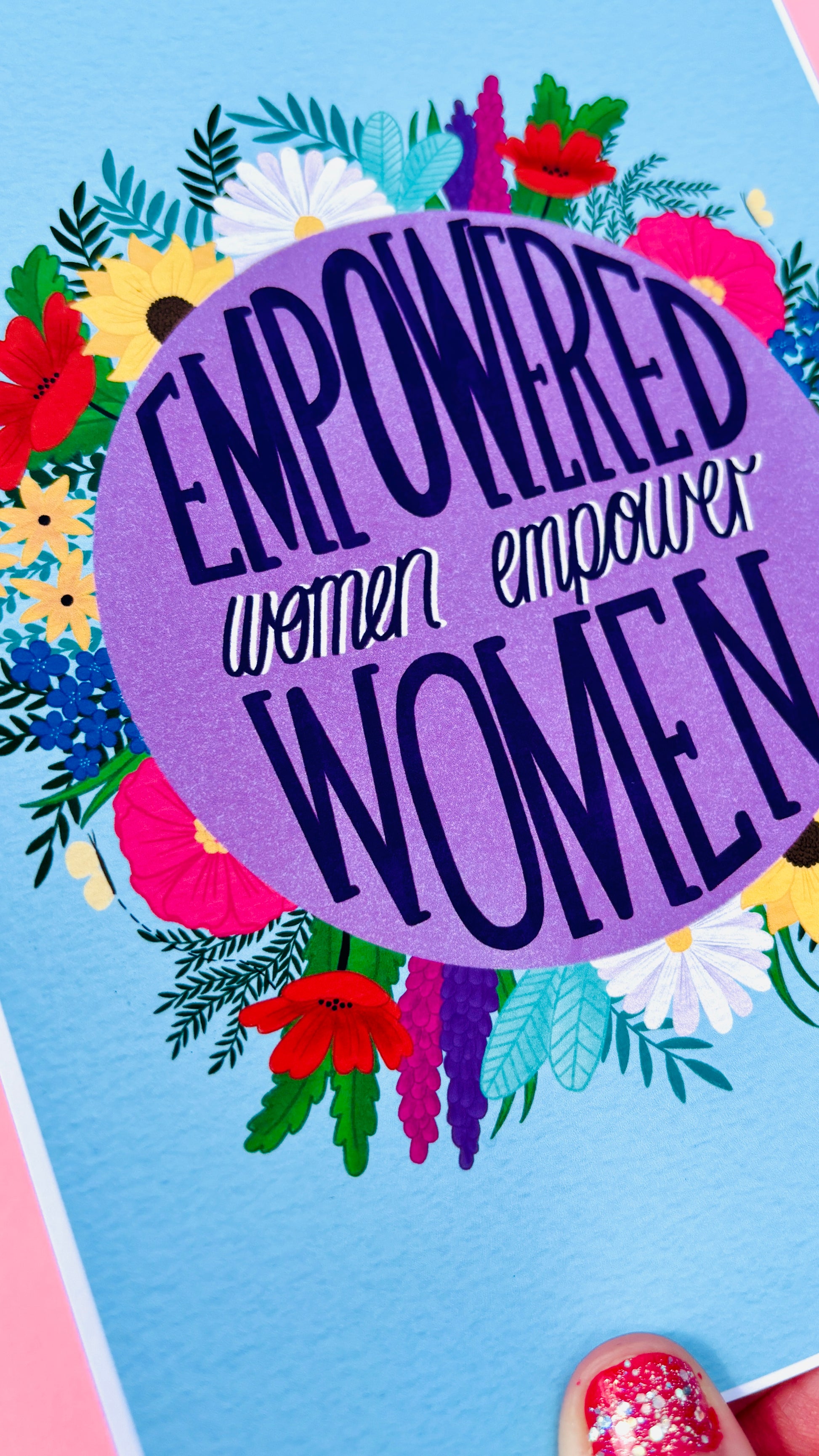 Feminist art print that reads “empowered women empower women” surround by colourful flowers and sets against a blue background. Inspirational wall art for women. 