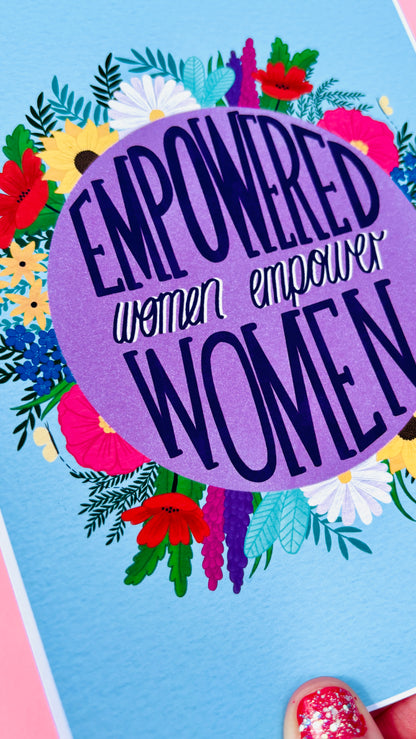 Feminist art print that reads “empowered women empower women” surround by colourful flowers and sets against a blue background. Inspirational wall art for women. 