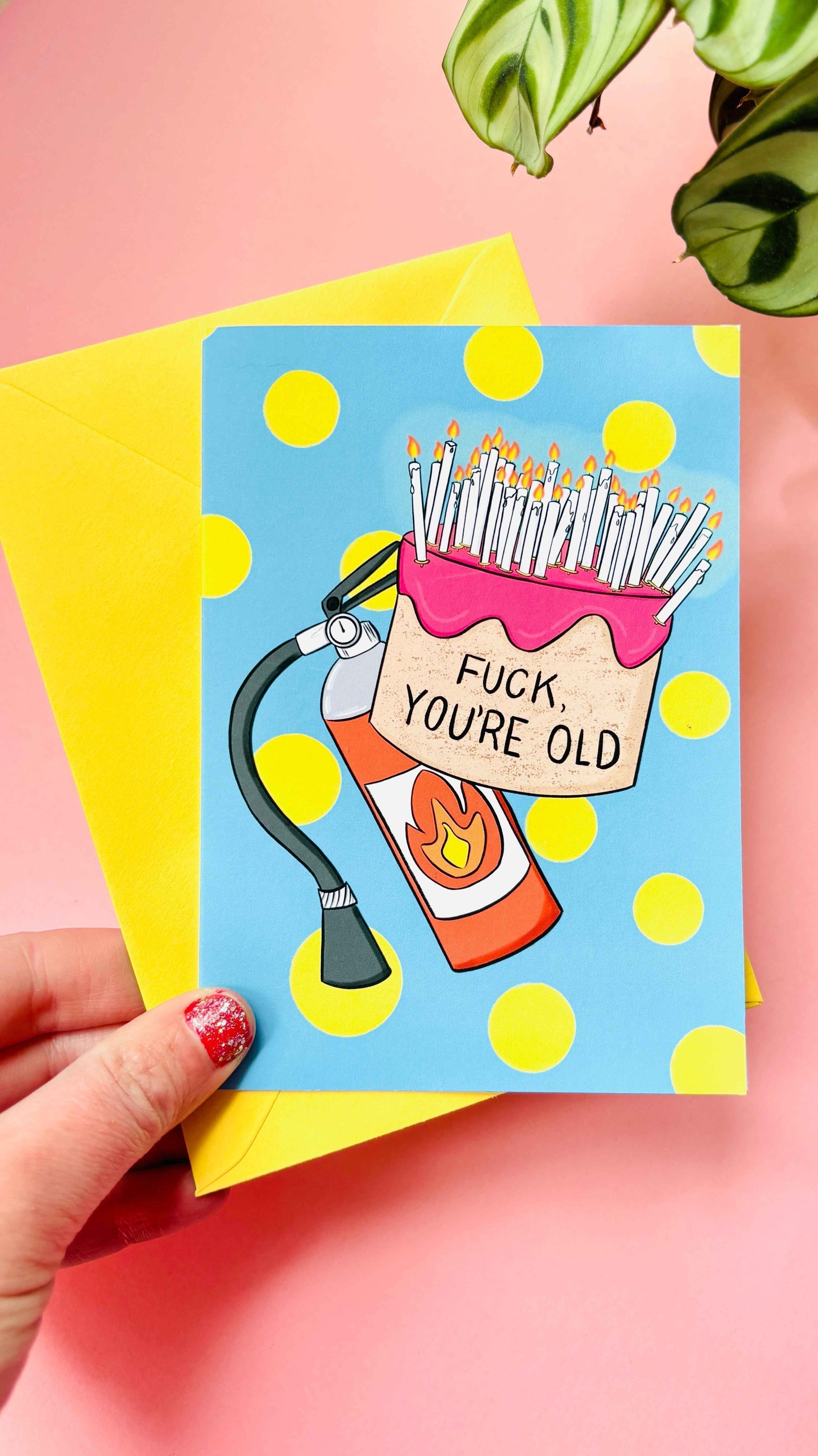 This handmade Sweary rude birthday card features a cake overflowing with candles and pre-cautionary fire extinguisher under the funny text “fuck you’re old” against a blue background with yellow polkadots 