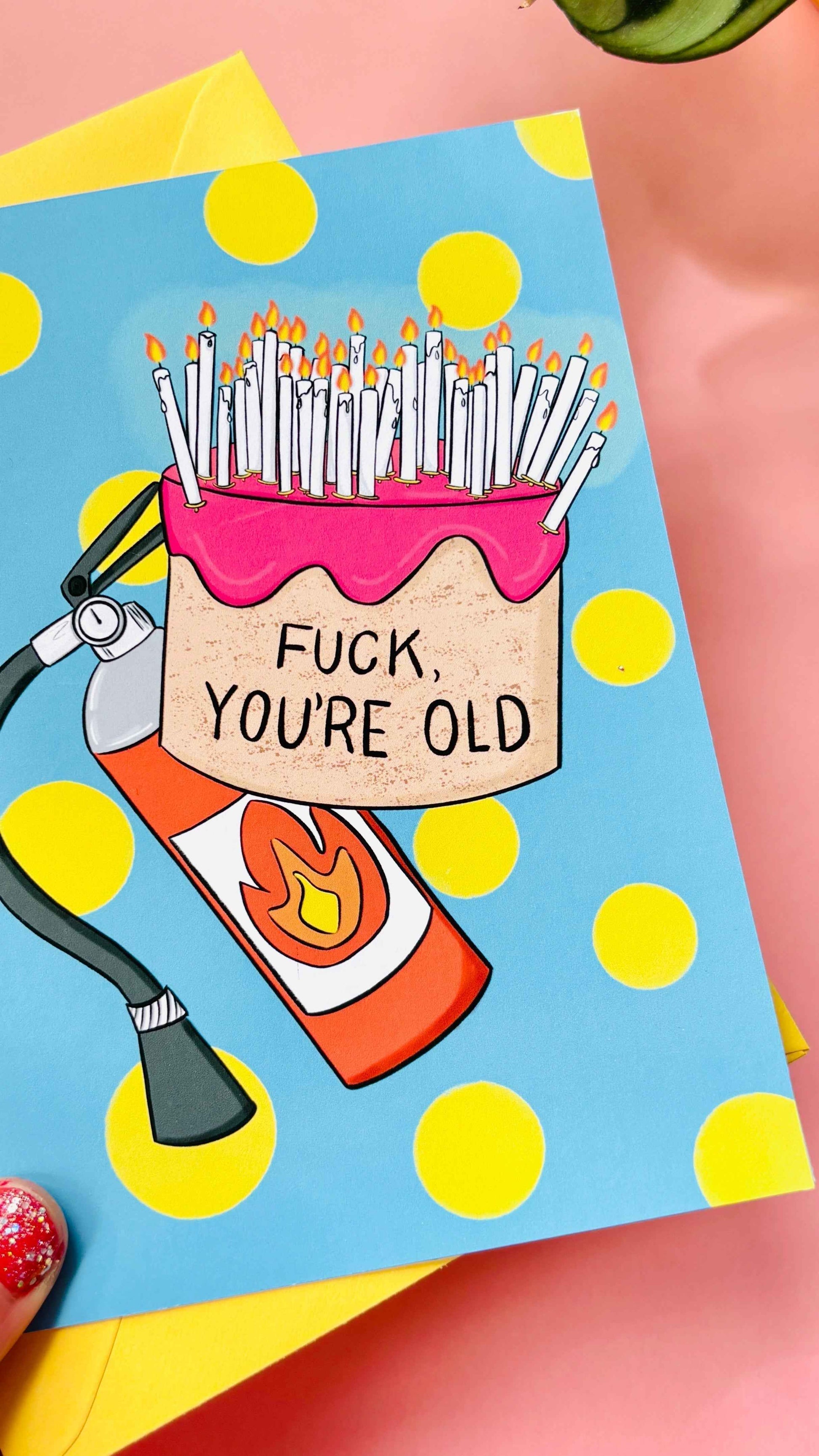 This handmade Sweary rude birthday card features a cake overflowing with candles and pre-cautionary fire extinguisher under the funny text “fuck you’re old” against a blue background with yellow polkadots 