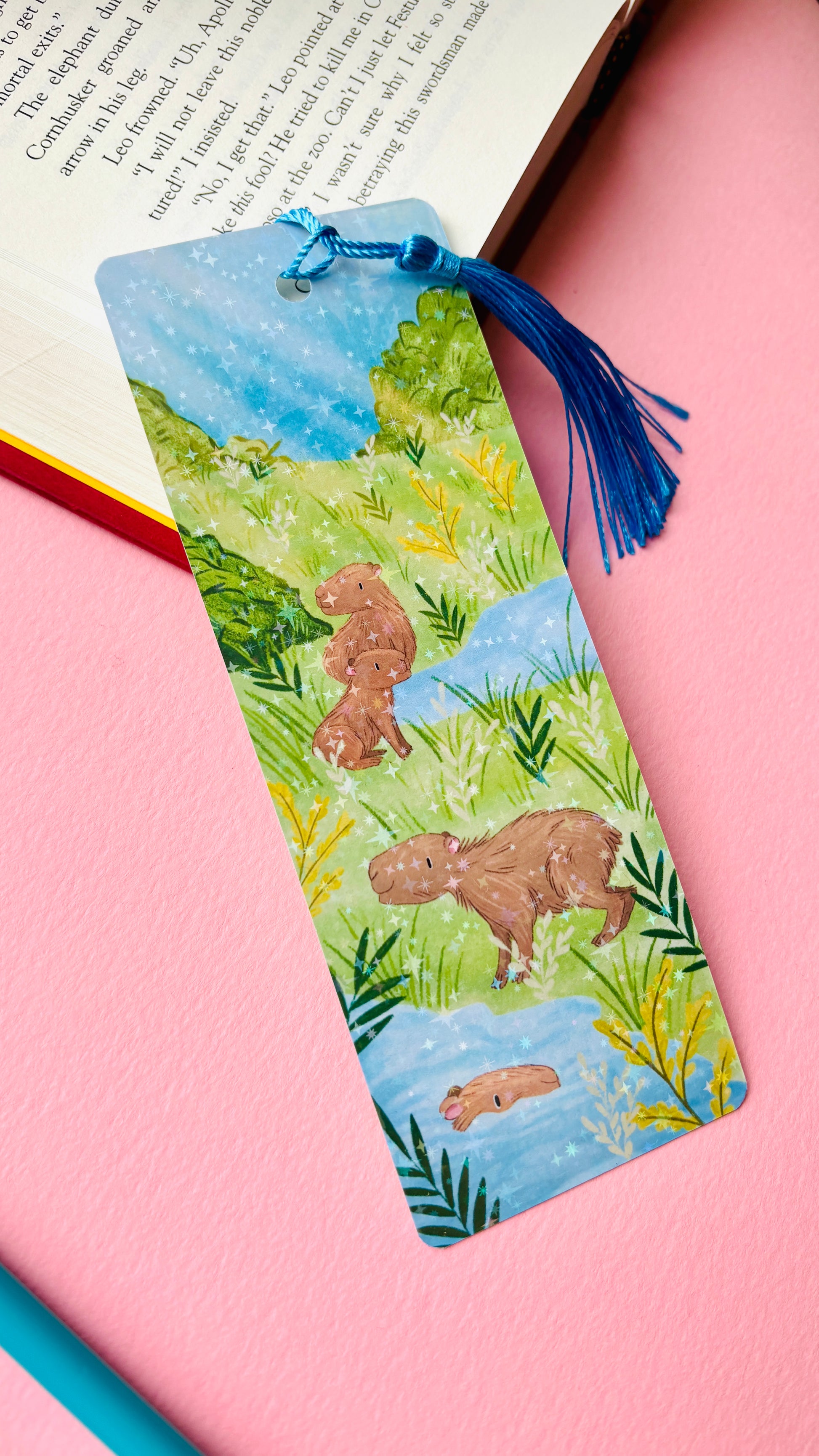 Illustrated bookmark with a capybara design with a rainbow holographic bookmark. 