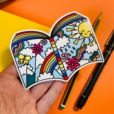 Colourful vinyl sticker of a book illustrated with rainbows, sunshine, mountains and butterflies