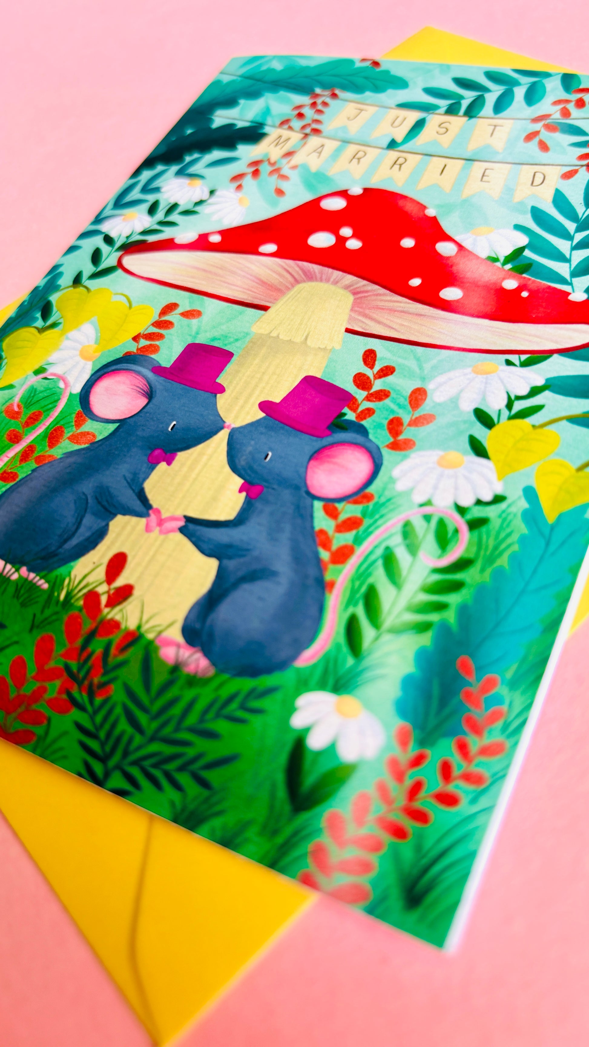 Cute gay wedding card of two mice under a whimsical toadstool in a vibrant woodland setting full of flowers and plants. This handmade card is blank on the inside for your message a d supplied with a yellow envelope 