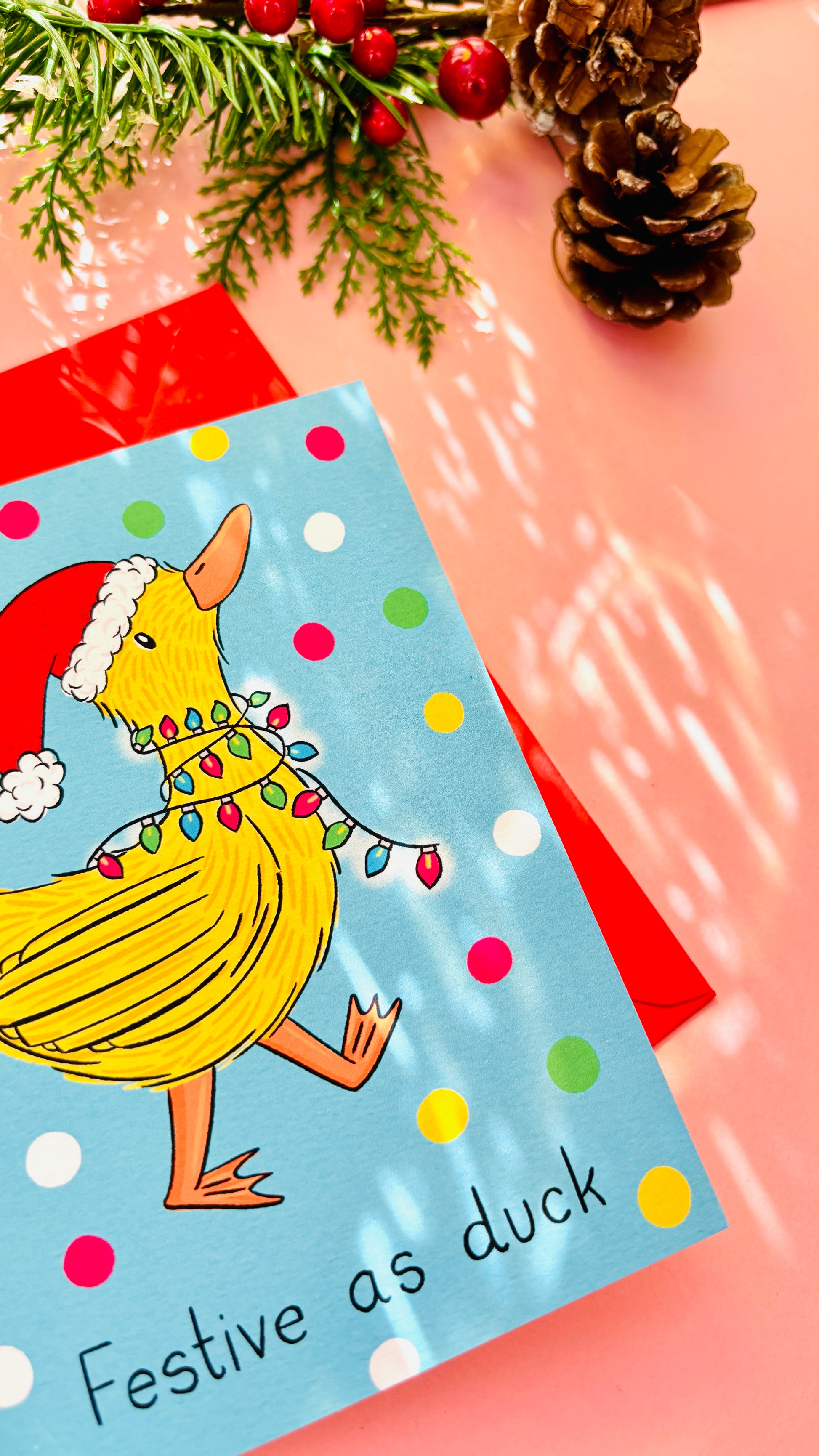 Cheeky holiday card featuring a bright yellow duck wearing a Santa hat, surrounded by colorful fairy lights on a blue polka dot background.