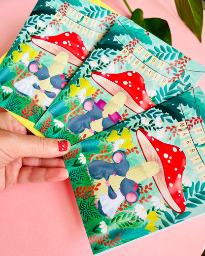 Handmade wedding card with a fantasy forest theme of two mice under a whimsical toadstool in a vibrant woodland setting full of flowers and plants. This handmade card is blank on the inside for your message a d supplied with a yellow envelope 