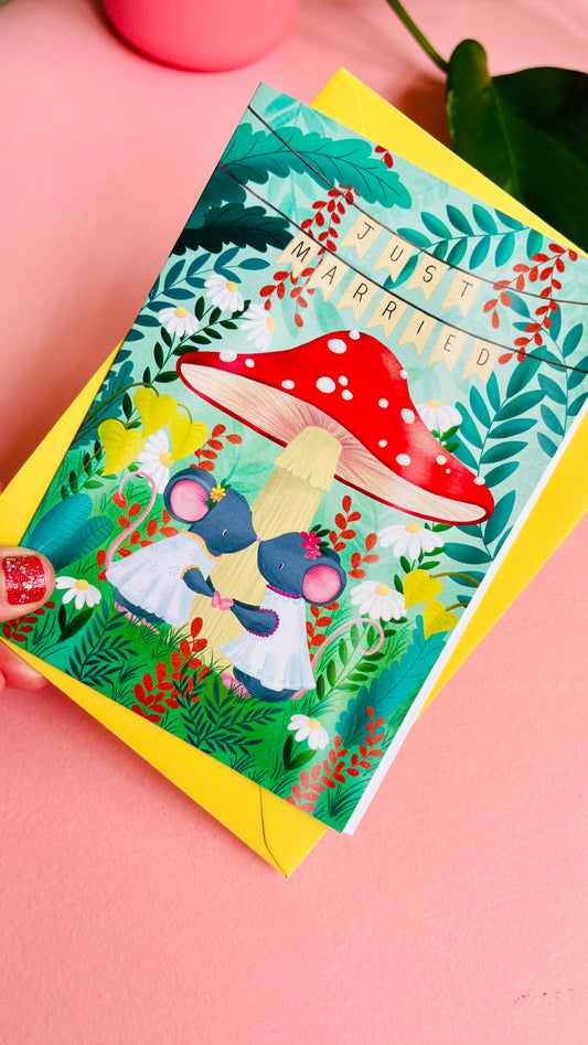 Handmade lesbian wedding card of two mice under a whimsical toadstool in a vibrant woodland setting full of flowers and plants. This handmade card is blank on the inside for your message a d supplied with a yellow envelope 