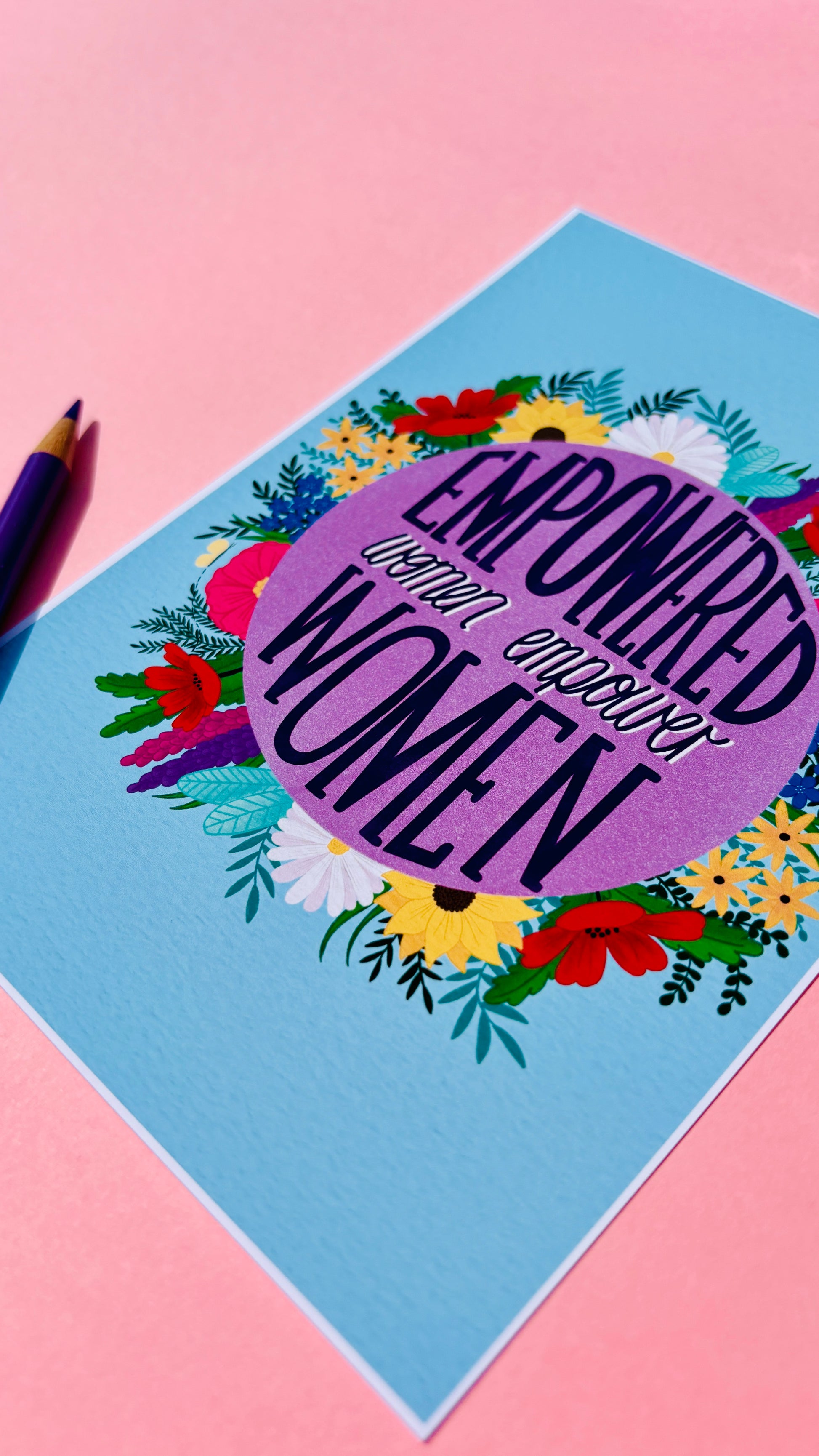 Feminist art print that reads “empowered women empower women” surround by colourful flowers and sets against a blue background. Inspirational wall art for women. 