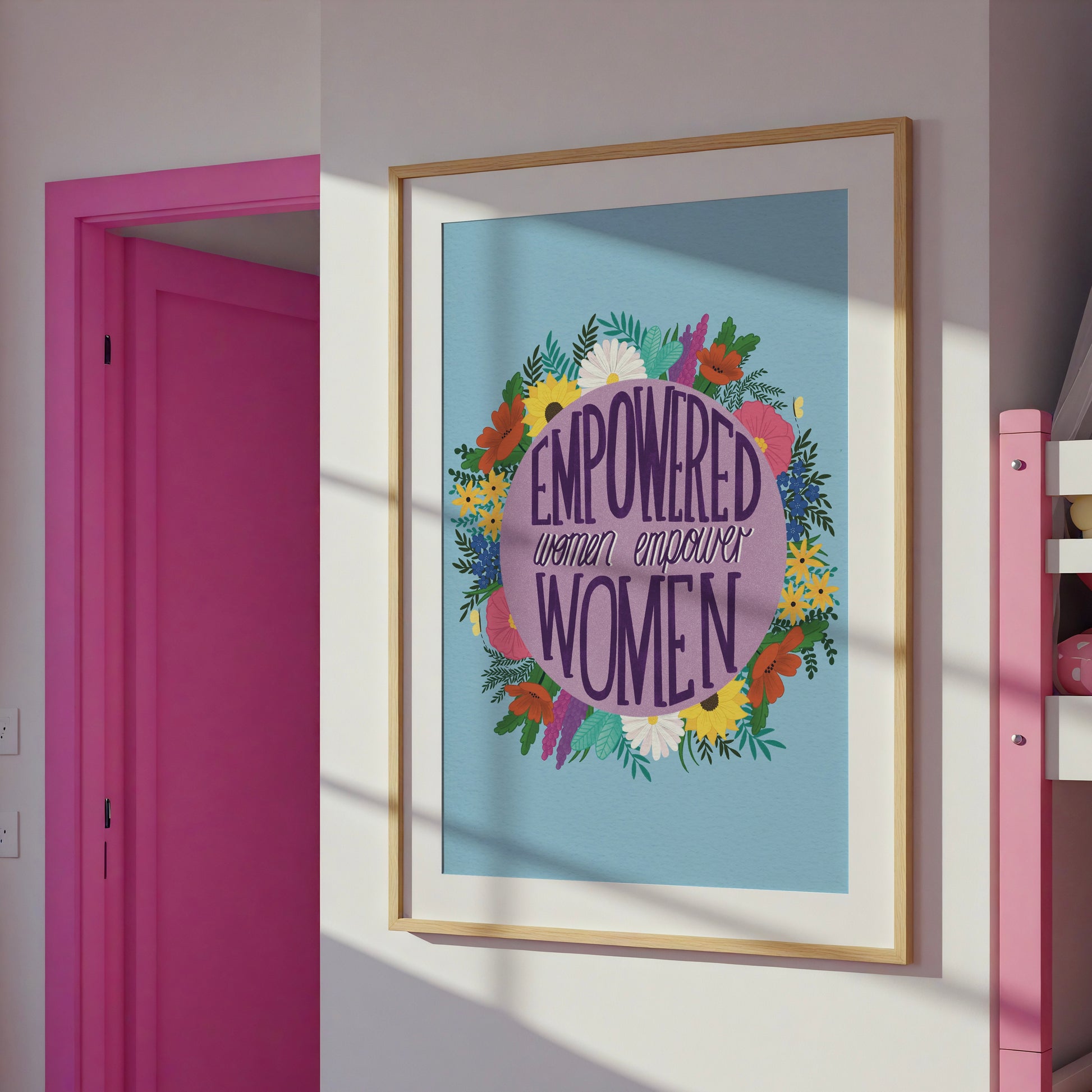 Feminist art print that reads “empowered women empower women” surround by colourful flowers and sets against a blue background. Inspirational wall art for women. 