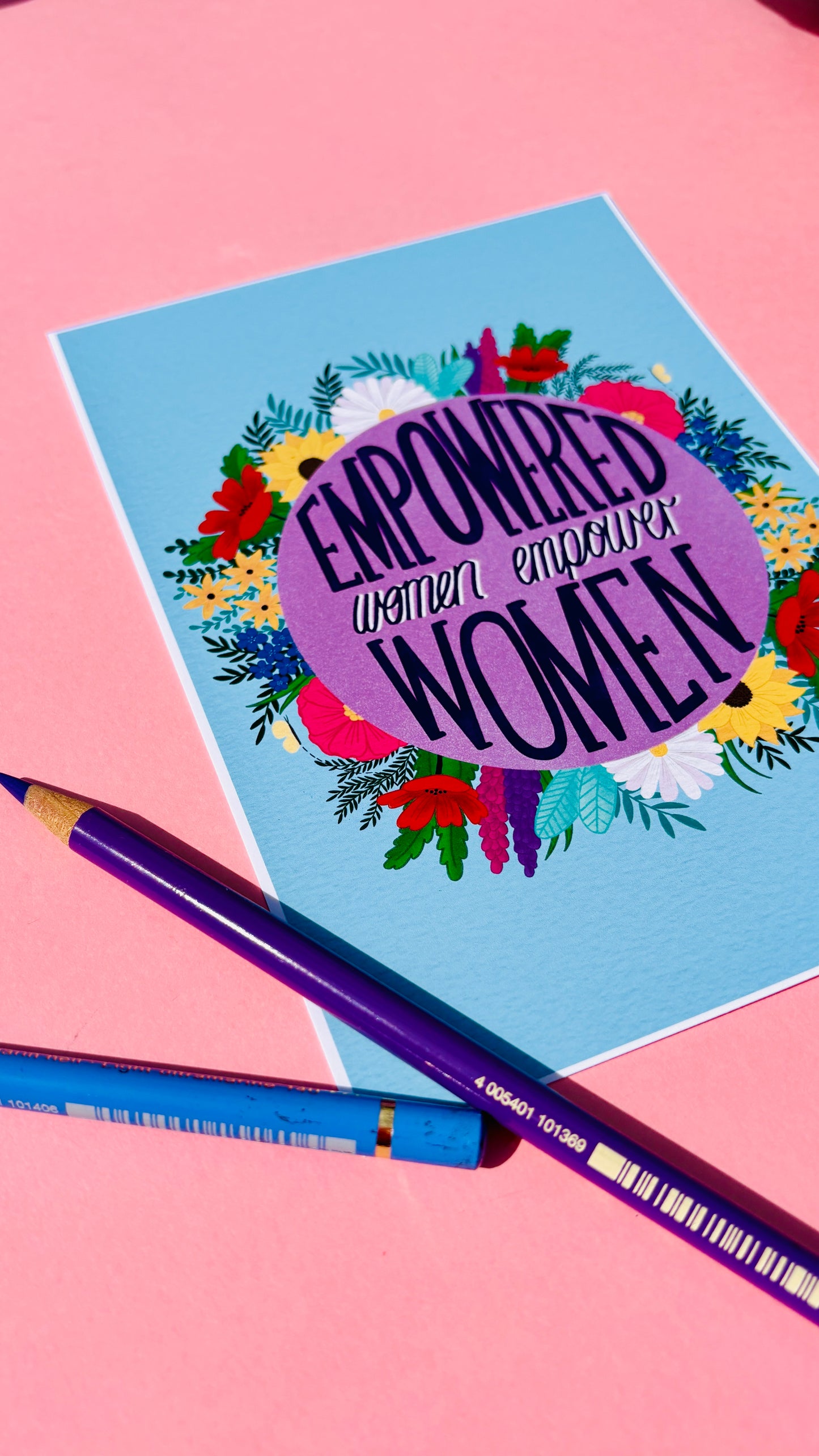 Feminist art print that reads “empowered women empower women” surround by colourful flowers and sets against a blue background. Inspirational wall art for women. 
