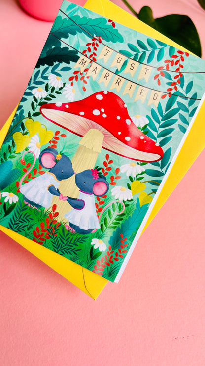 Handmade lesbian wedding card of two mice under a whimsical toadstool in a vibrant woodland setting full of flowers and plants. This handmade card is blank on the inside for your message a d supplied with a yellow envelope 