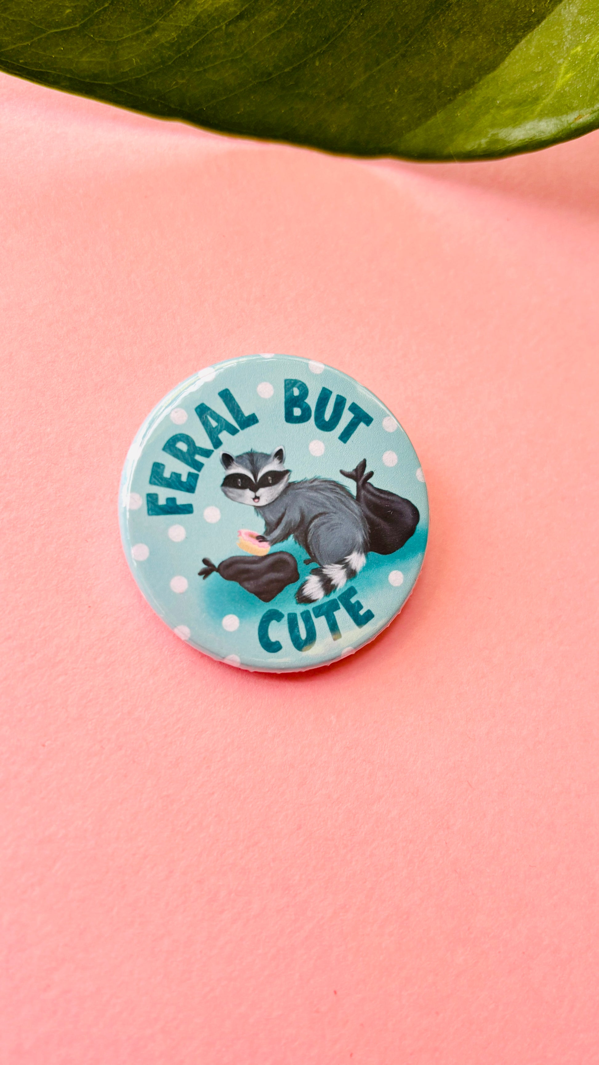 Cute hand-illustrated raccoon badge or magnet with “Feral but Cute” text, handmade in the UK – fun gift for wildlife lovers and quirky accessory collectors.

