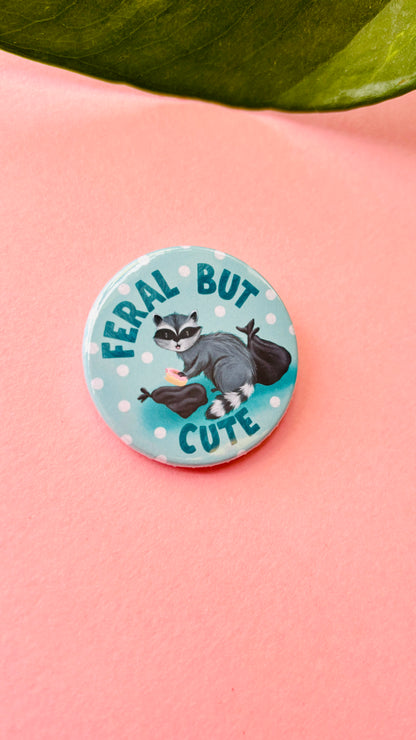 Cute hand-illustrated raccoon badge or magnet with “Feral but Cute” text, handmade in the UK – fun gift for wildlife lovers and quirky accessory collectors.
