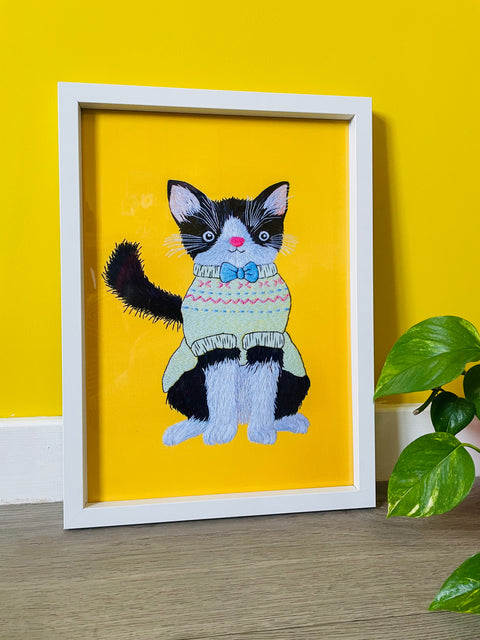 Colourful wall art of a black and white cat in a jumper on a bright yellow background
