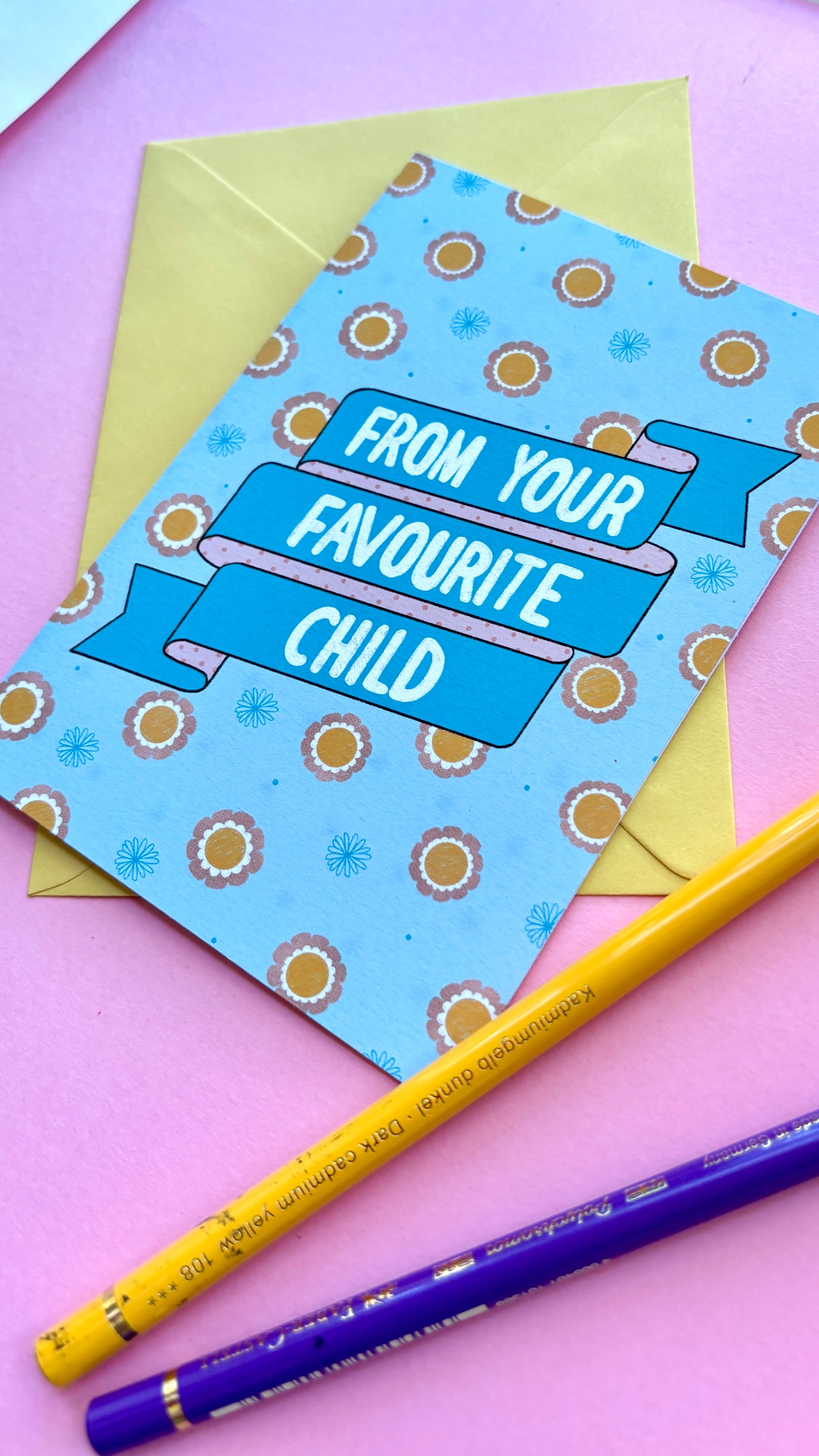 A funny handmade greetings card for mum or dad and reads “from your favourite child” on a blue and pink banner against a colourful retro feel floral background. Supplied with a yellow envelope.