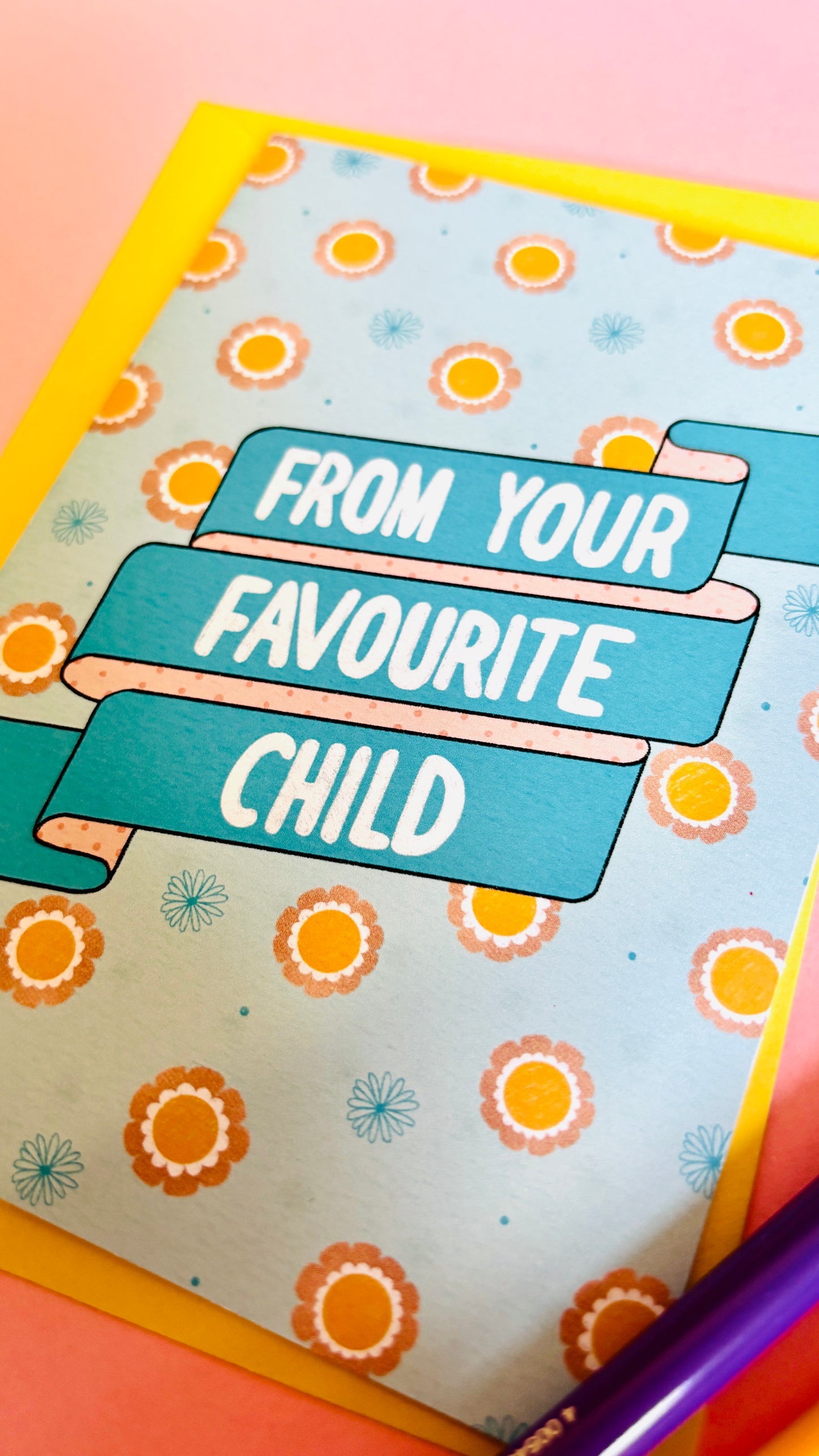 A funny handmade greetings card for mum or dad and reads “from your favourite child” on a blue and pink banner against a colourful retro feel floral background. Supplied with a yellow envelope.