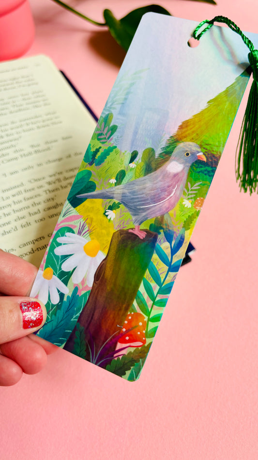 Handmade bookmark with cute pigeon art. This holographic bookmark features an adorable wood pigeon sitting on a mossy tree stump surrounded by colourful plants and flowers with a subtle cityscape in the background. Finished with a tassel, rounded corners and rainbow holographic laminate it makes a great gift for pigeon lovers and bookish besties. 