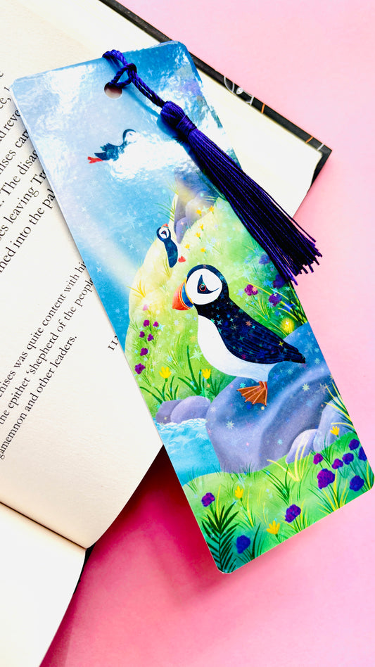 Handmade puffin bookmark with rainbow holographic finish, featuring a cute puffin on a colorful coastal seaside scene, FSC-certified paper, and coordinating tassel, perfect for book lovers and bird enthusiasts.
