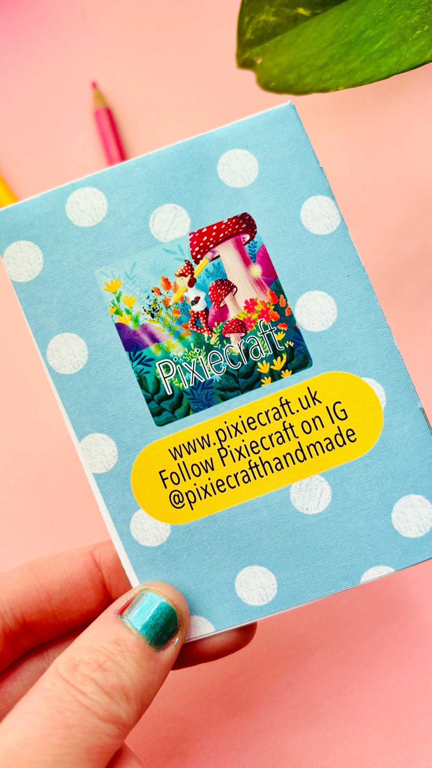 Hand holding a blue reverse of artist zine with white polka dots featuring a colorful design and text.