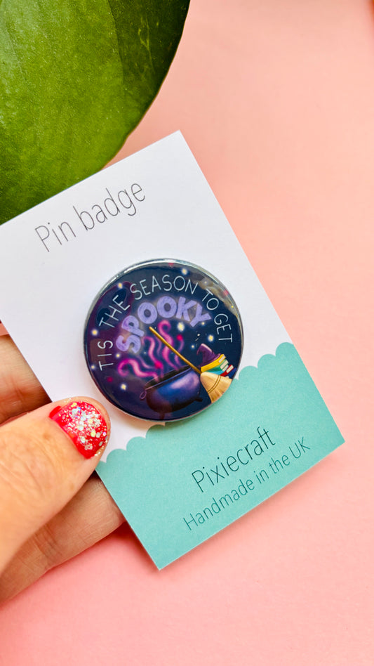 Halloween badge or magnet reading “Tis the Season to Get Spooky” with cauldron and broom illustration, hand-illustrated and festive accessory.