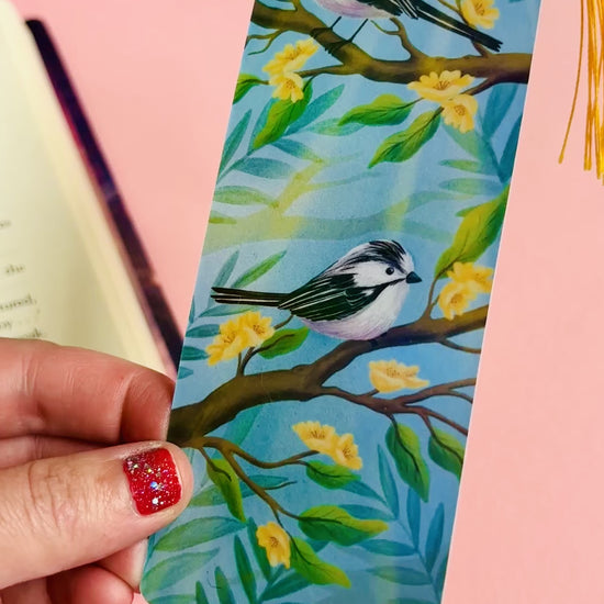 Handmade bookmark with illustration of two cute long tailed tits sitting on delicate branches surrounded by yellow flowers. Finished with rainbow holographic laminate, rounded corners and a tassel. Ideal gift for bookish gifts lovers. 