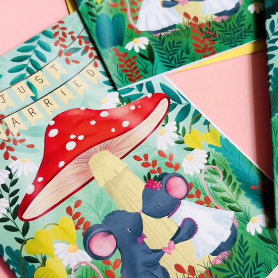 Cute gay wedding card of two mice under a whimsical toadstool in a vibrant woodland setting full of flowers and plants. This handmade card is blank on the inside for your message a d supplied with a yellow envelope 