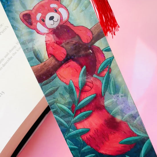 Cute red panda bookmark featuring a whimsical illustration, rainbow holographic laminate, and green tassel, perfect for animal lovers and avid readers.