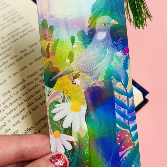 Handmade bookmark with cute pigeon art. This holographic bookmark features an adorable wood pigeon sitting on a mossy tree stump surrounded by colourful plants and flowers with a subtle cityscape in the background. Finished with a tassel, rounded corners and rainbow holographic laminate it makes a great gift for pigeon lovers and bookish besties. 