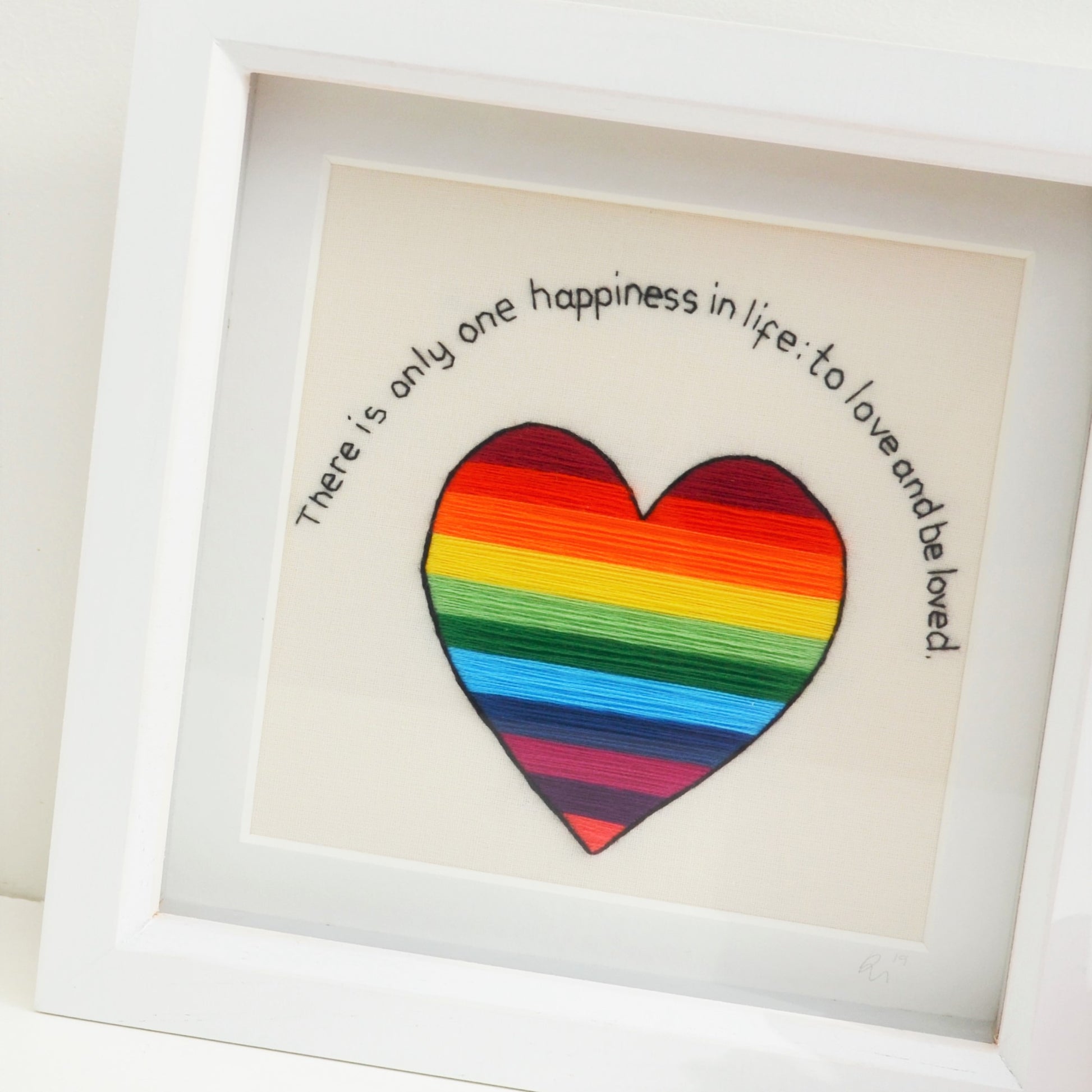 A close up view of a rainbow striped heart underneath the text There is only one happiness in life: to love and be loved